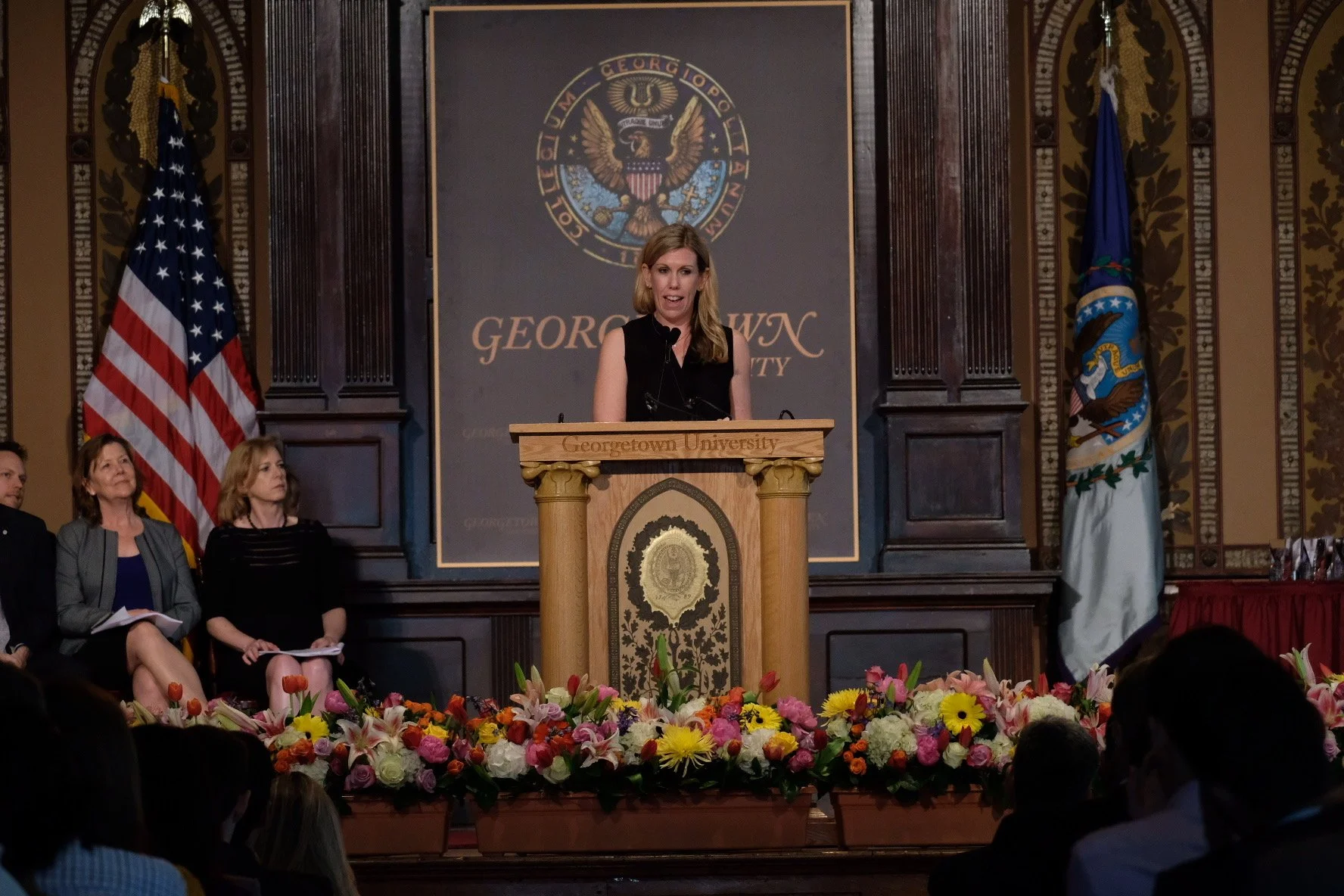 A woman, Brooke Van Dam, standing at a lectern at Georgetown University giving a speech.