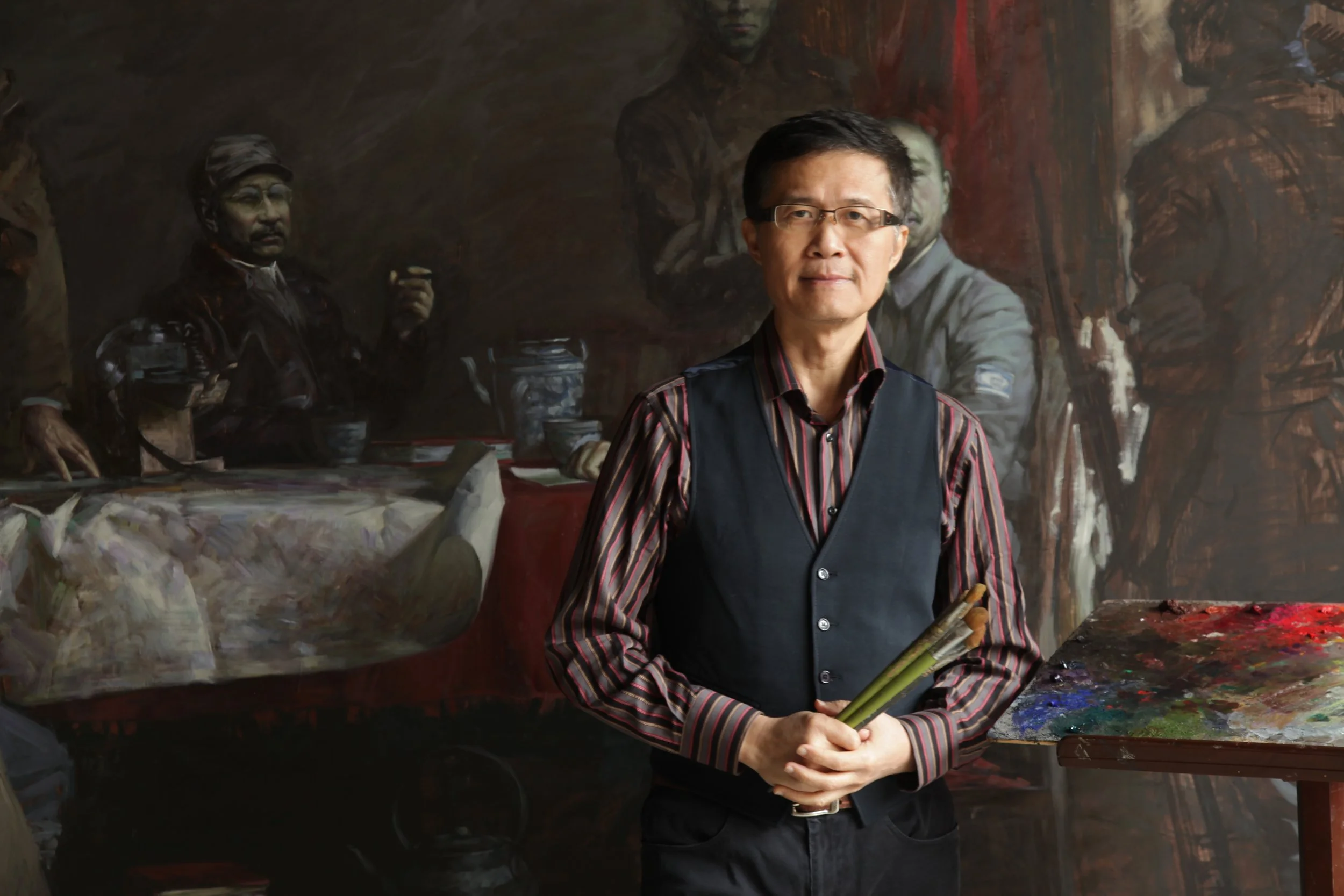 Portrait of artist Ming Qin in his studio holding paintbrushes.