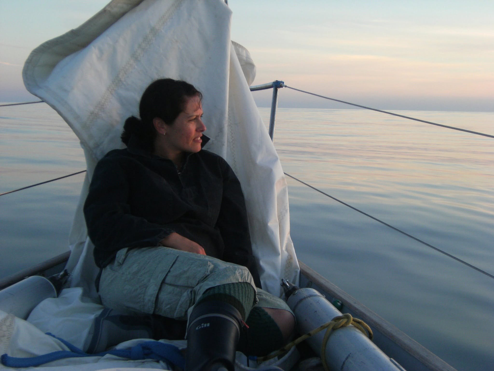 A woman relaxing on a boat with a calm ocean and a sunset sky in the background.