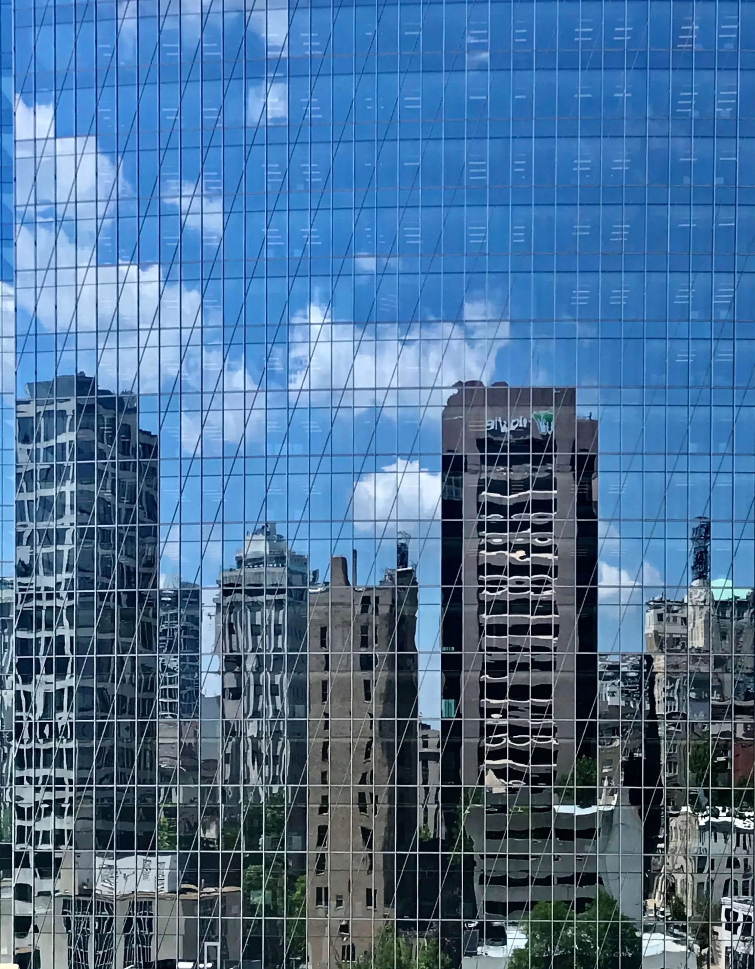 Skyscraper's mirrored glass facade reflecting distorted city buildings in Richmond, Virginia and clouds, cable-supported window grid visible.