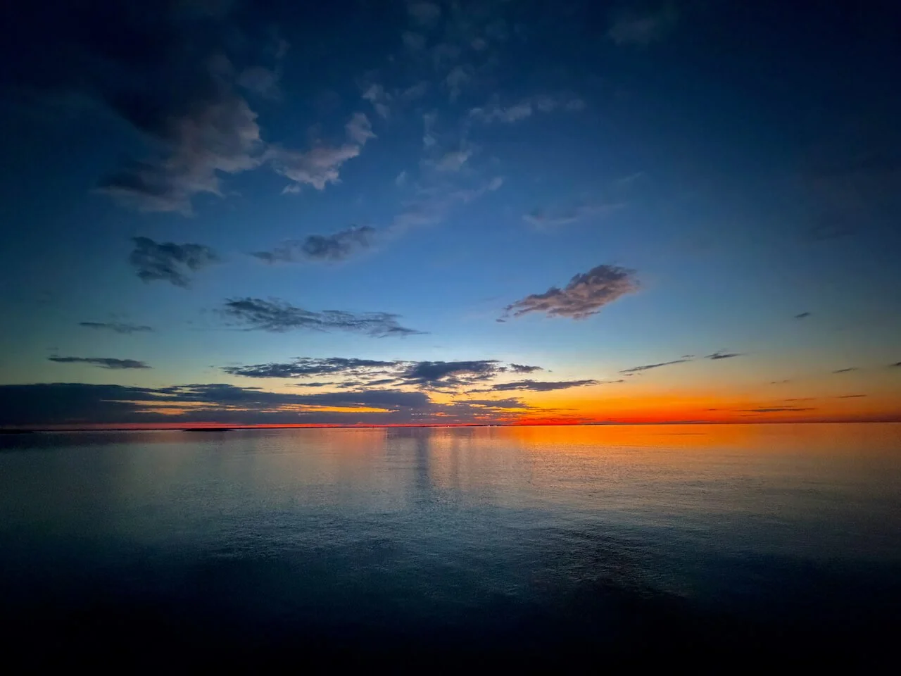 Daybreak over the calm Potomac, orange horizon fading into deep blue sky with scattered clouds.