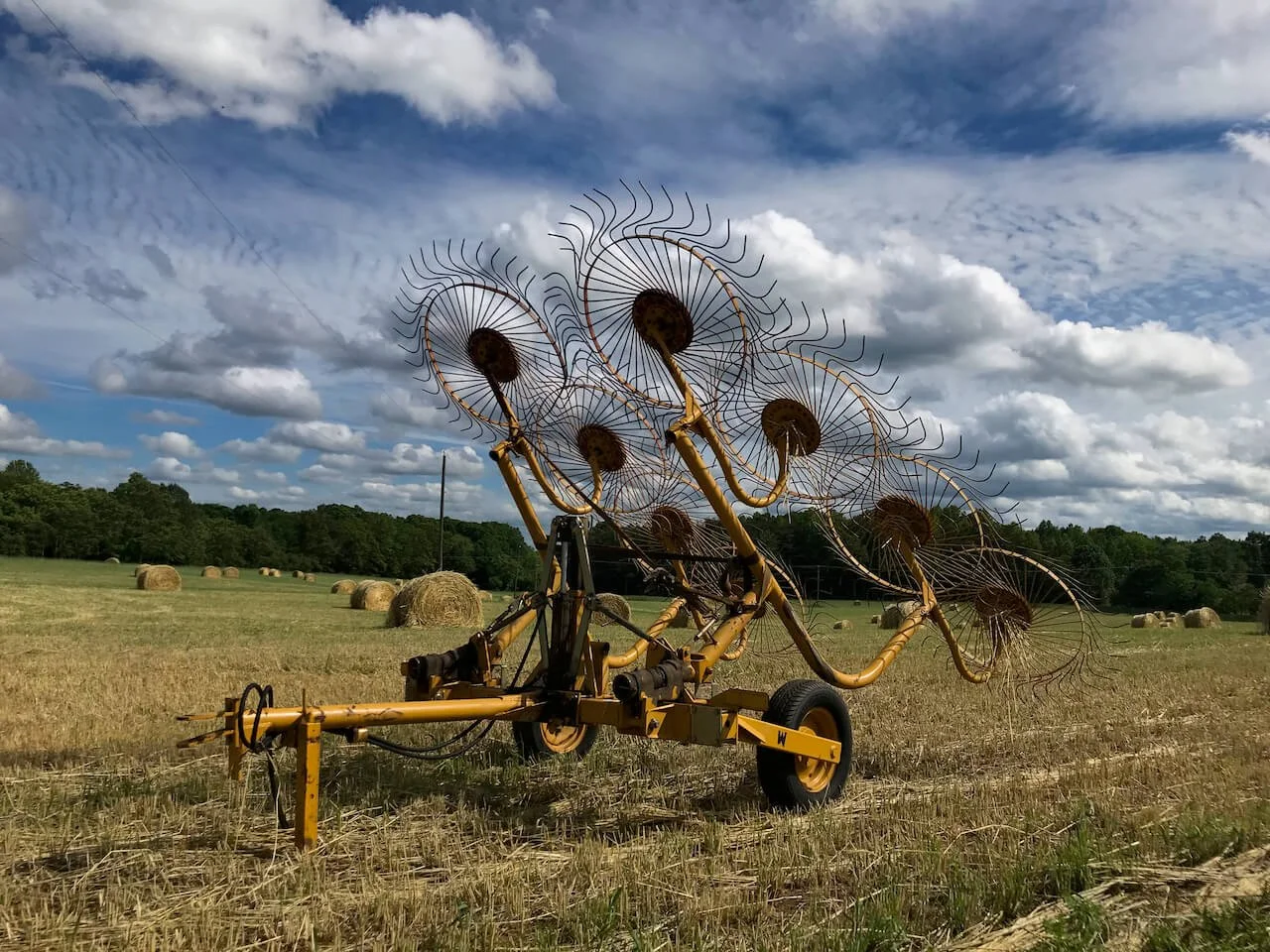 Yellow wheel hay rake in a mown field, Cumberland County, Virginia, hay bales and blue sky