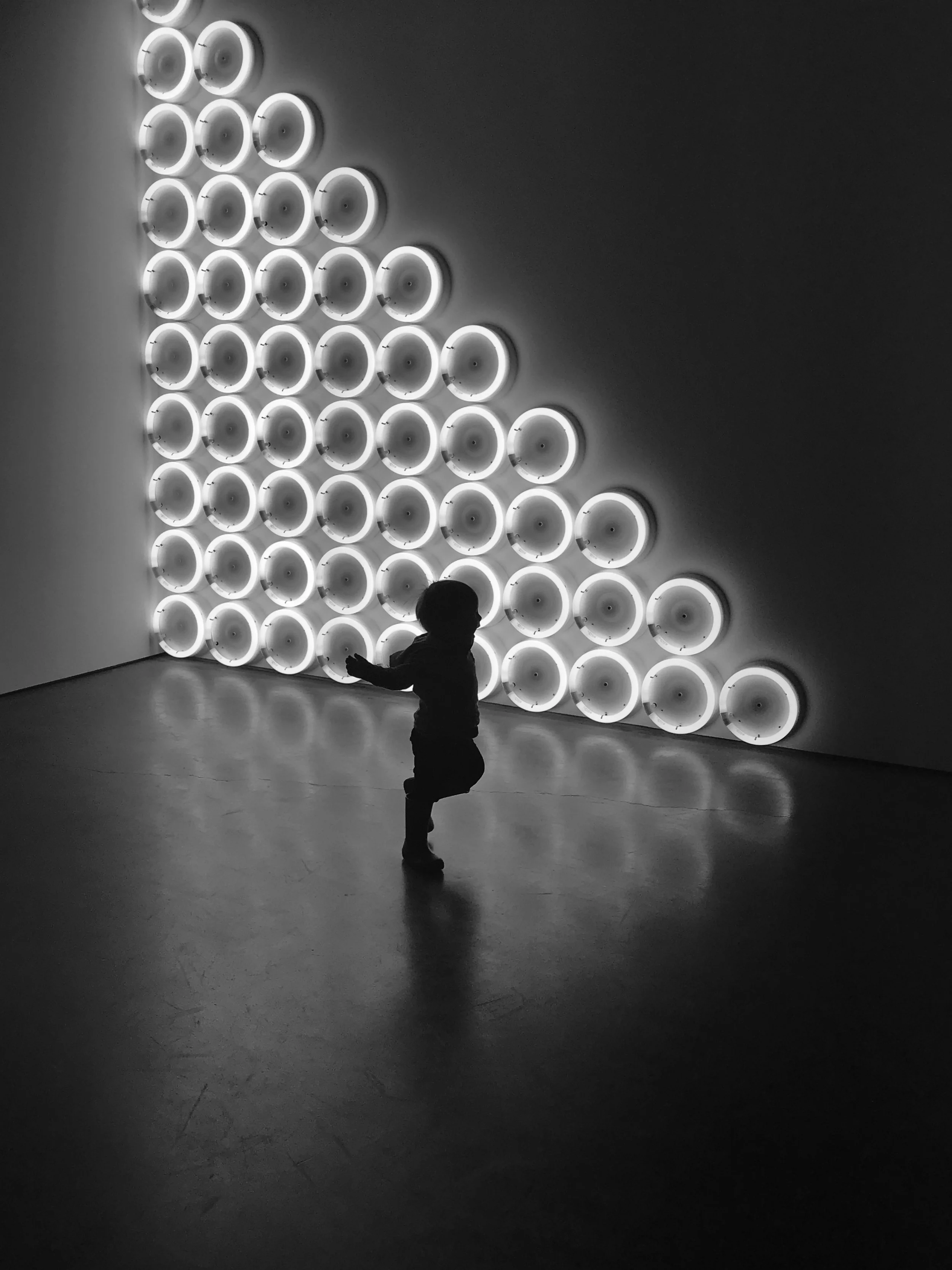 Black-and-white photo of a child silhouetted before a triangular grid of illuminated circular lights