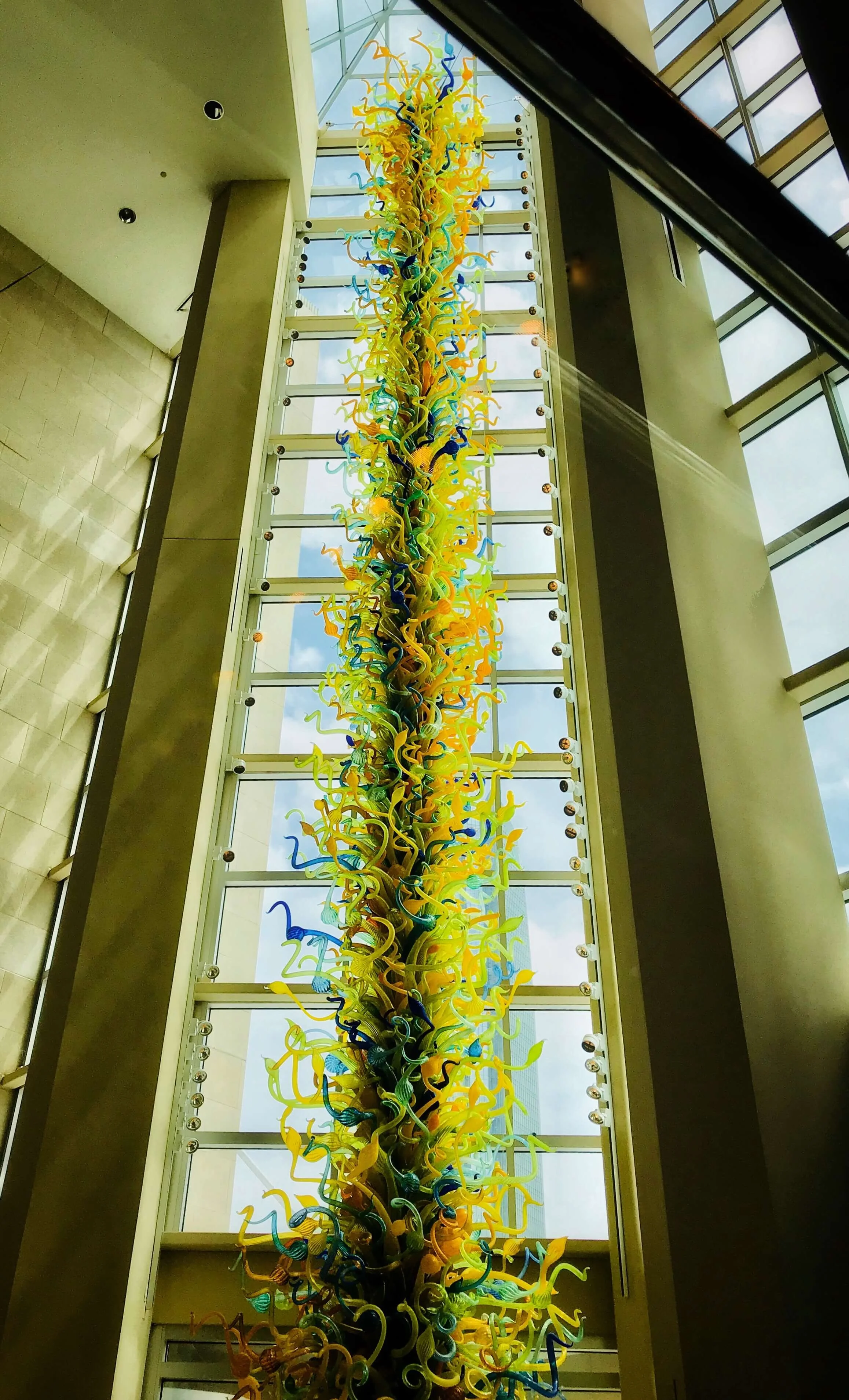 Eleanor Blake Kirkpatrick Memorial Tower by Dale Chihuly at the Oklahoma City Museum of Art. Tall glass art tower standing in tall paned window with sunlight streaming in from behind