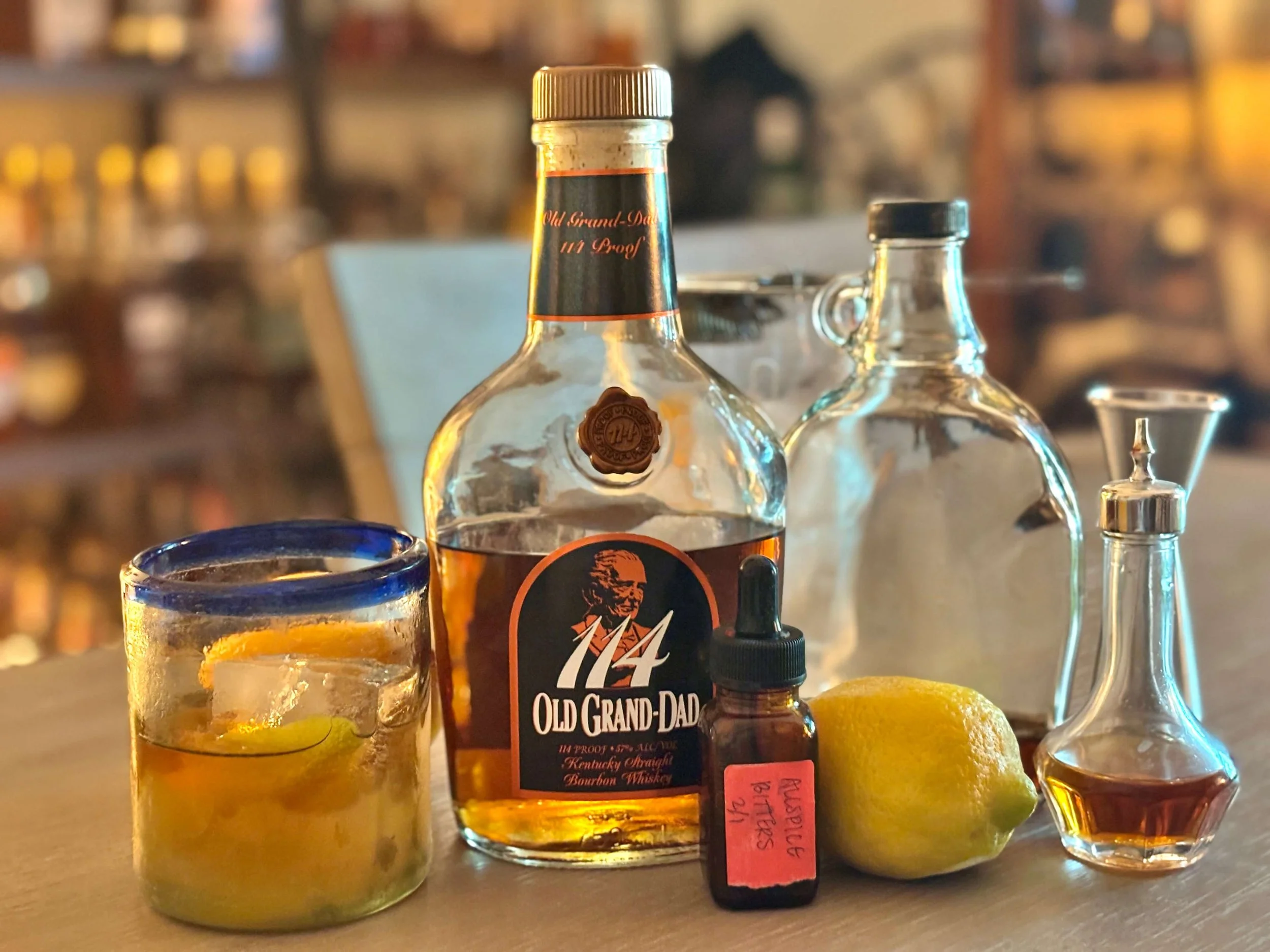 The Old Fashioned Granddad with Ingredients for the cocktail laid out: Old Grand-dad 114 bourbon, allspice and orange bitters, lemon, demerara syrup.