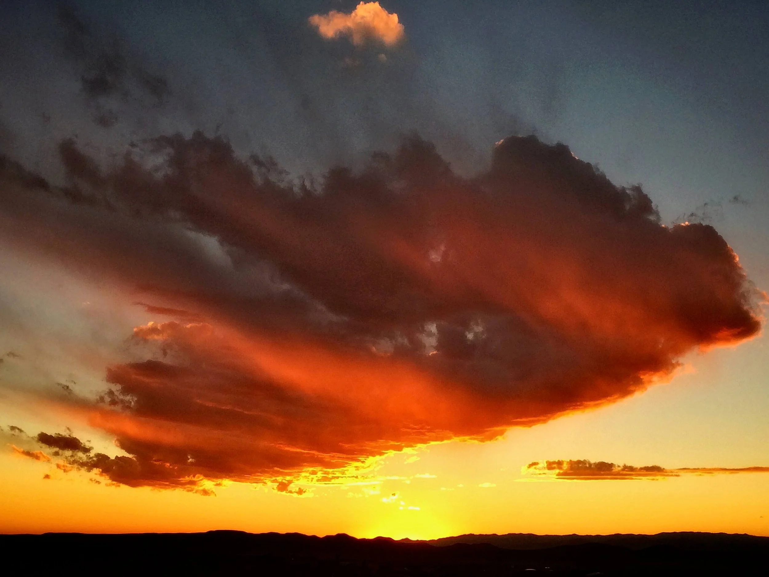 A vibrant sunset sky in Santa Fe, New Mexico with dark cloud unfurled in orange, yellow, and pink hues over the Jemez Mountains.