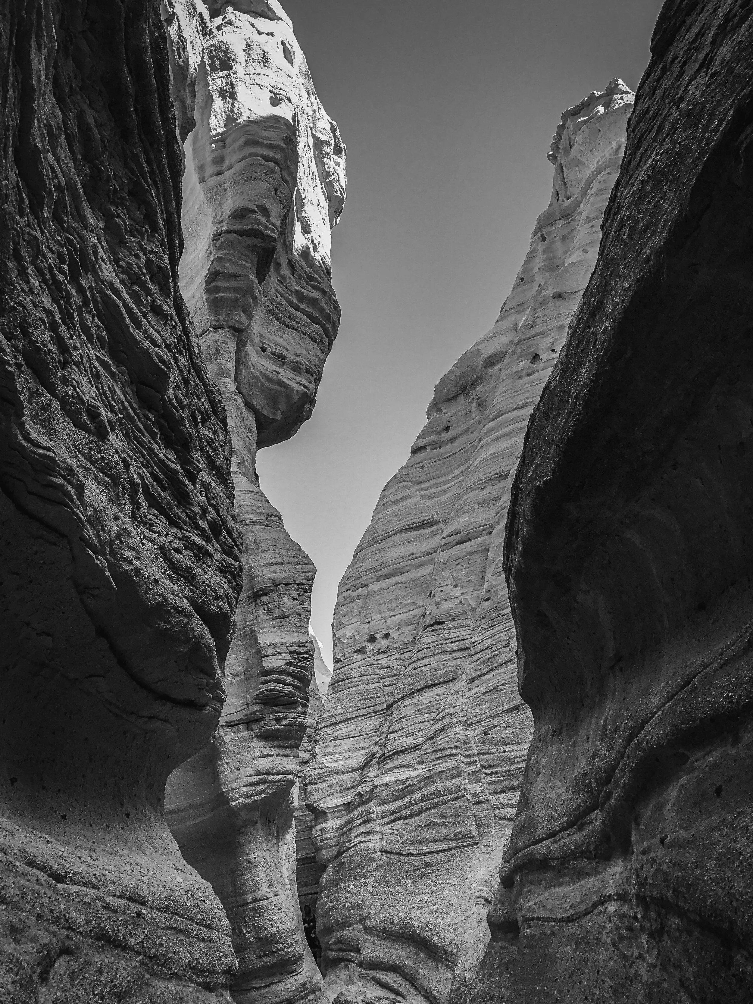 Black and white photo of narrow canyon walls with layered, textured rock formations, showing a winding trail through the slot canyon at Kasha-Kutuwe Tent Rocks in New Mexico.