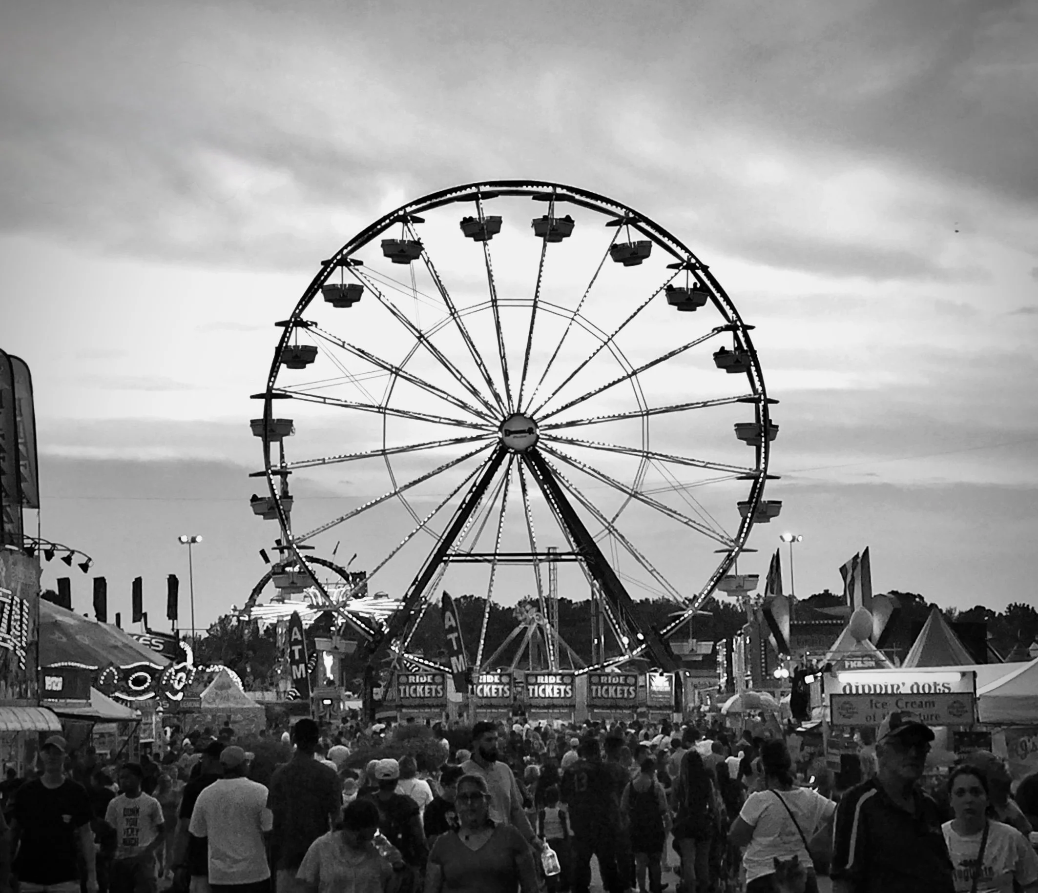 Black-and-white photo of a ferris wheel at the Virginia State Fair, towering over a crowded midway at dusk