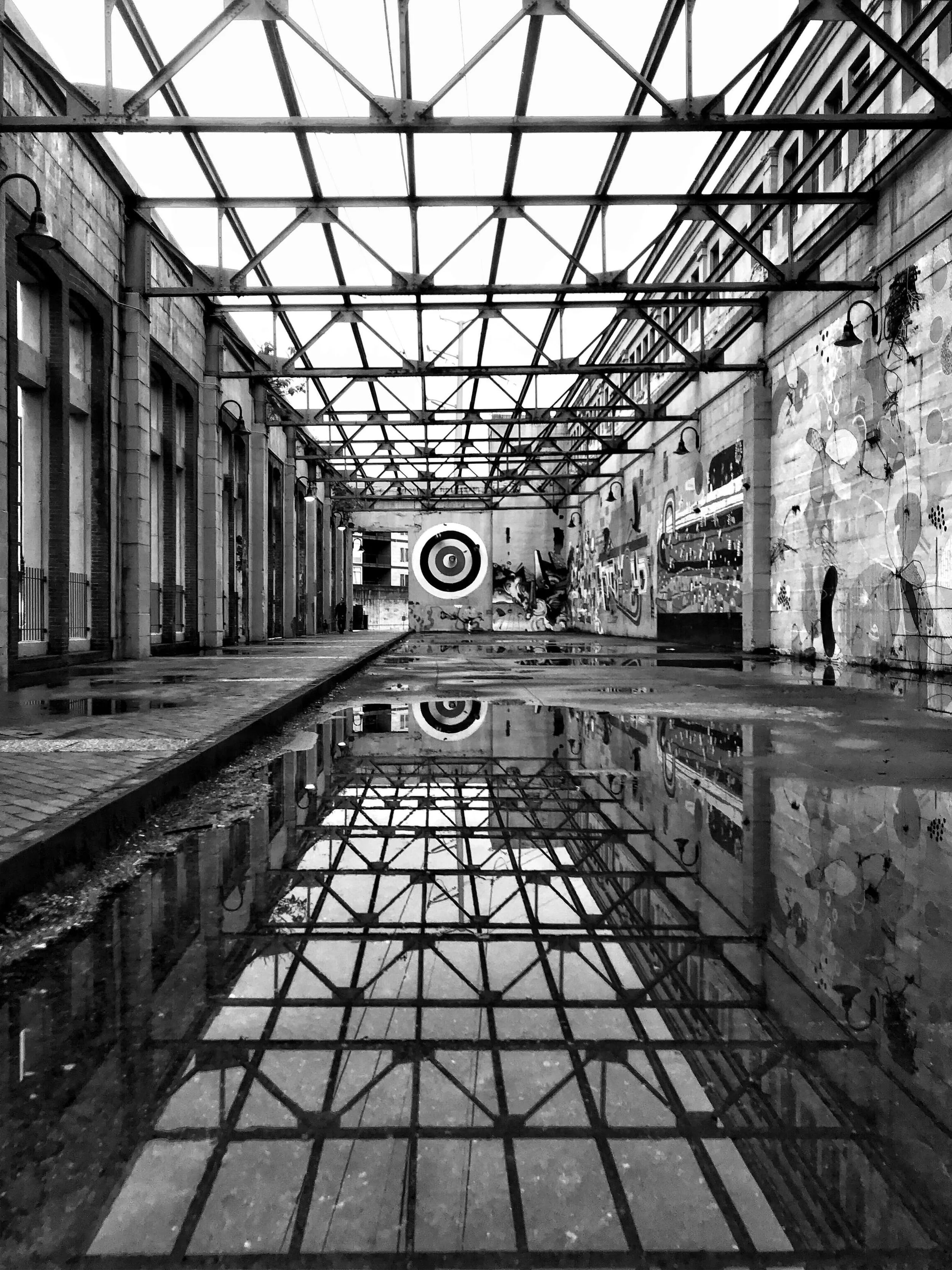 Graffiti wall showing a painted bullseye in black and white with metal girders reflecting in pooled water below and in open air along the Canal Walk in Richmond, Virginia