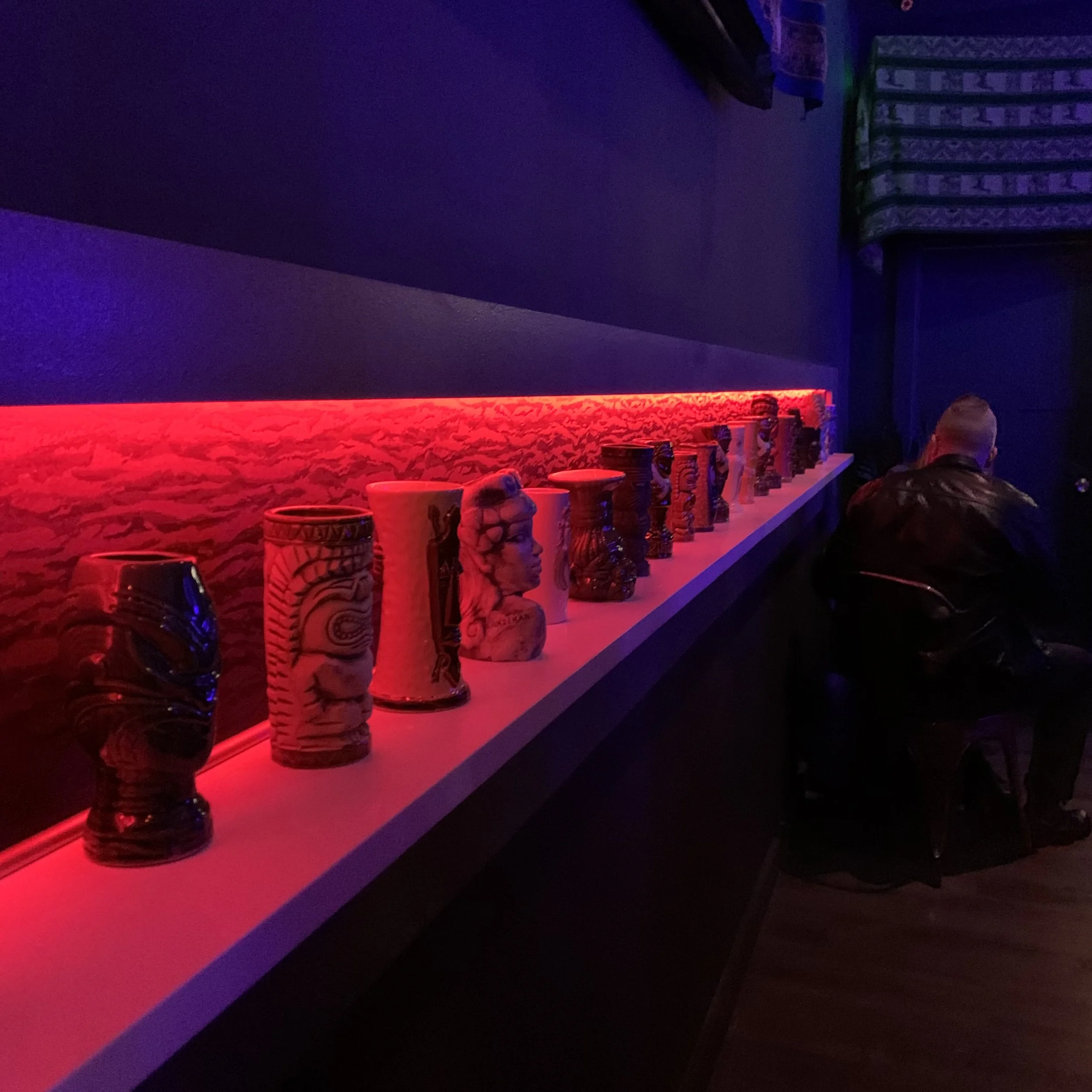 A bar or lounge with a red lit counter and decorative vases on display, featuring a dark blue and purple color scheme.
