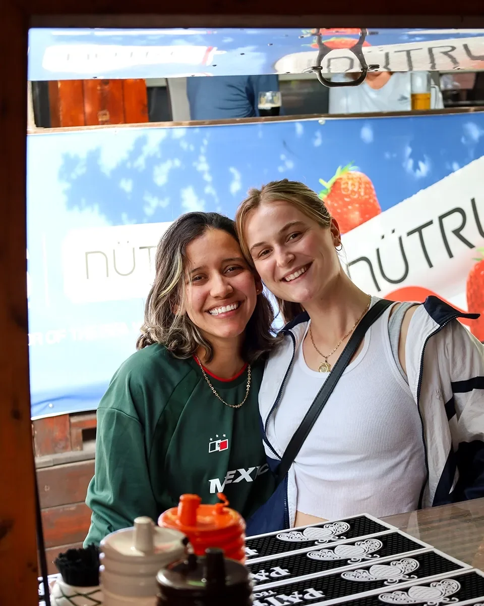 Two women smiling and taking a photo together at a table, with a Nutri sign and strawberries in the background.