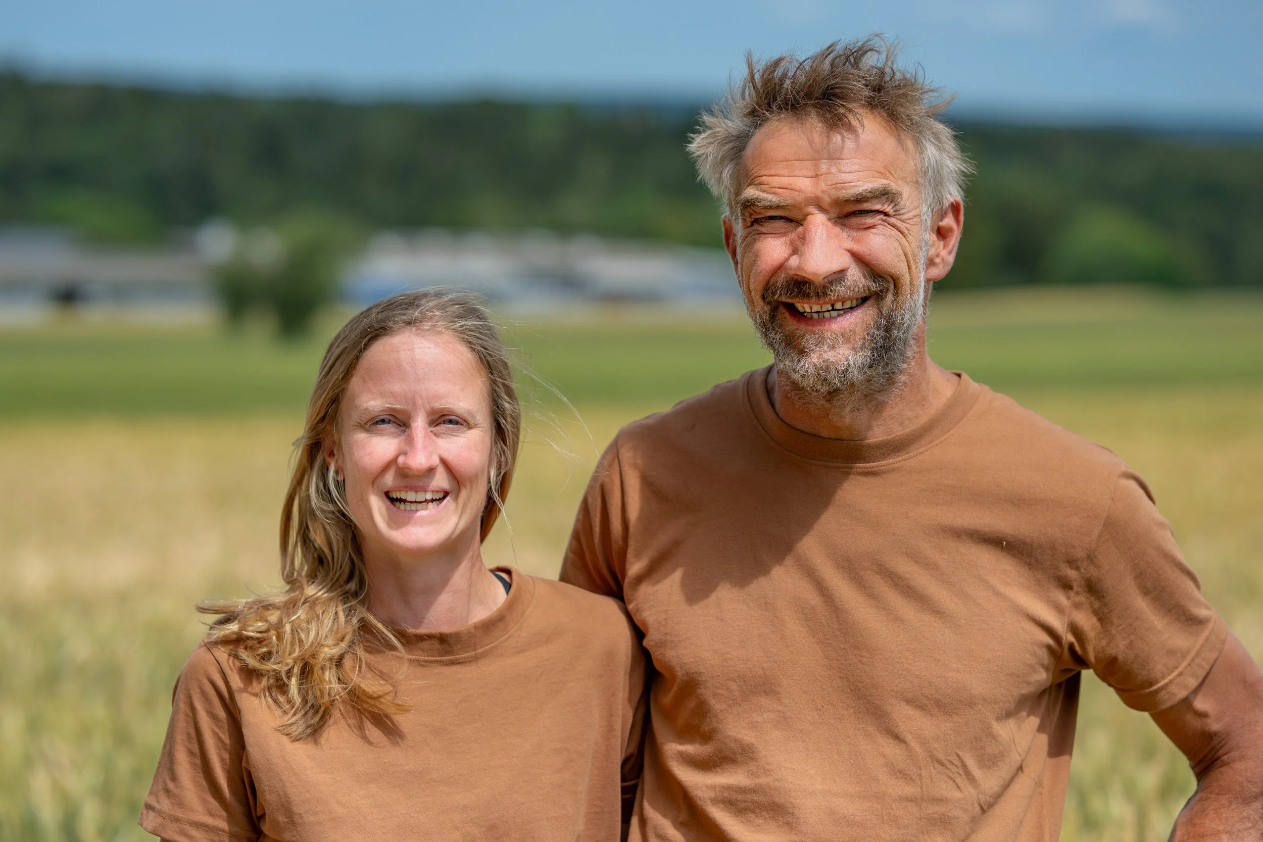 Lächelndes Paar in braunen T-Shirts vor einer ländlichen Landschaft