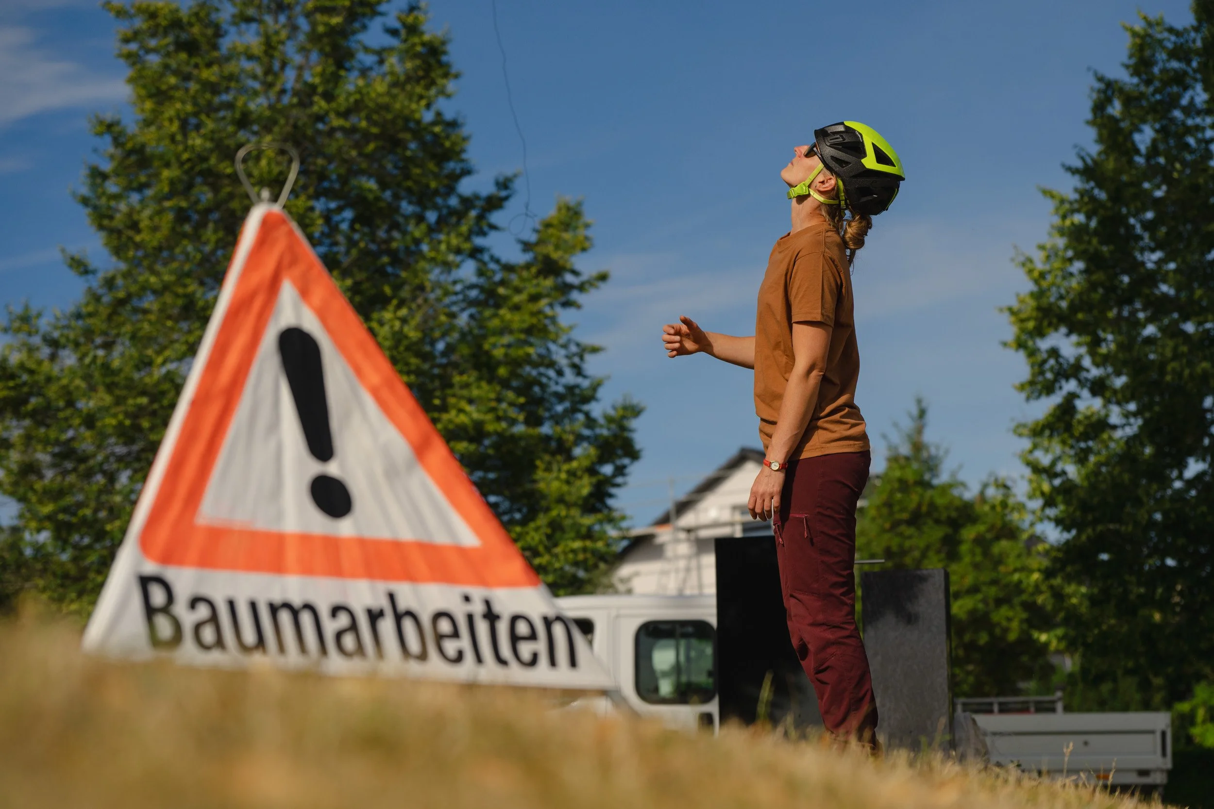 Radfahrerin mit grünem Fahrradhelm neben einem Warnschild „Baumarbeiten“ auf einer Baustelle