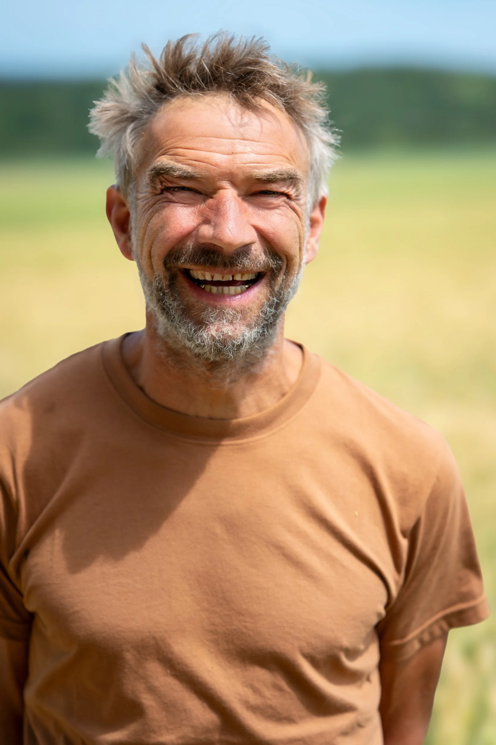 Fröhlicher älterer Mann mit grauem Bart und zerzaustem Haar lächelt im Freien.