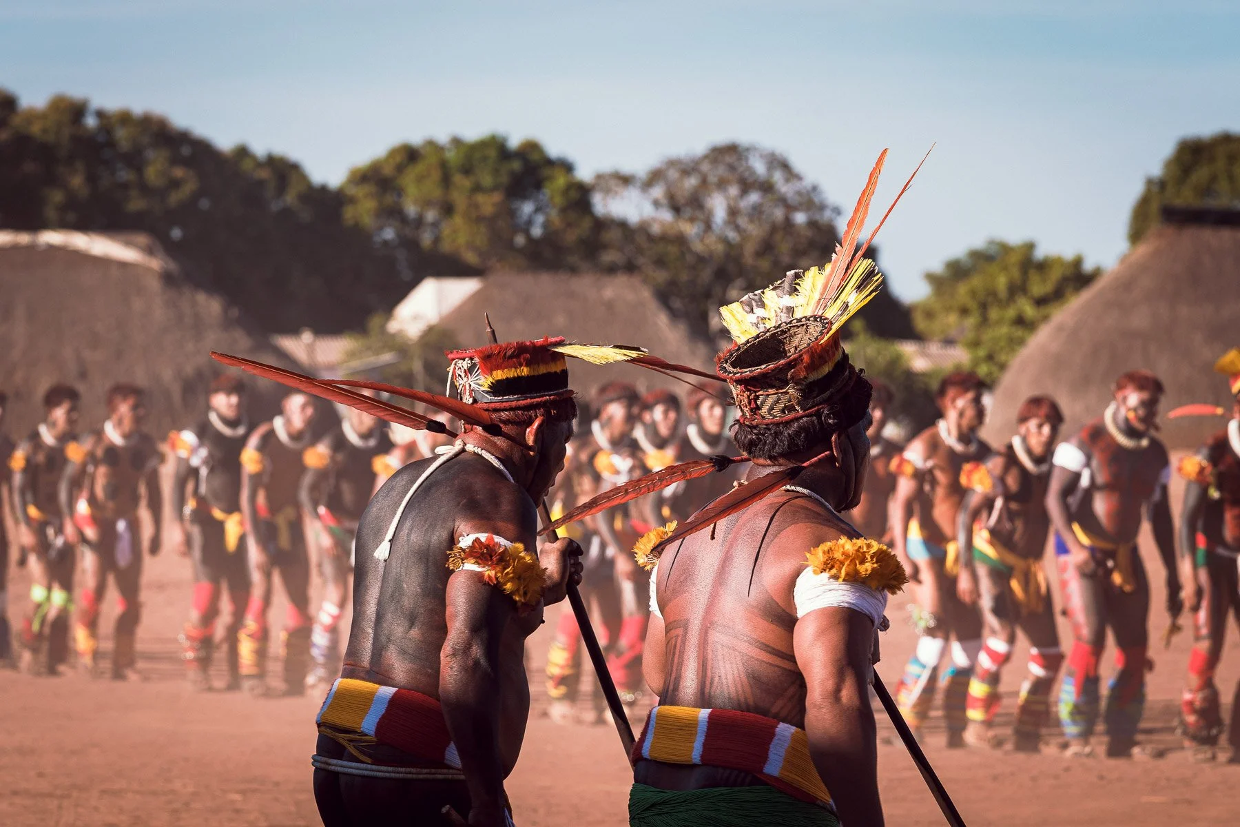 Hommes en tenue traditionnelle dans un rassemblement culturel en Afrique, avec des danseurs en arrière-plan.