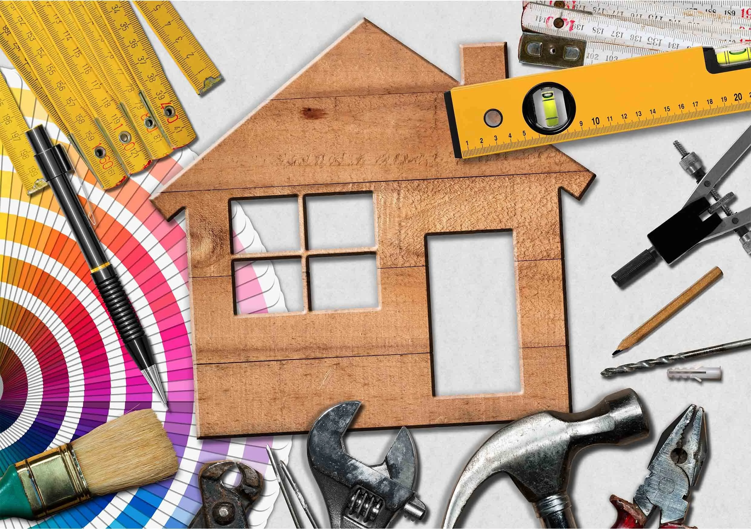 A wooden house-shaped cutout, surrounded by various construction tools and materials, including rulers, a level, a paintbrush, a wrench, and a color wheel.