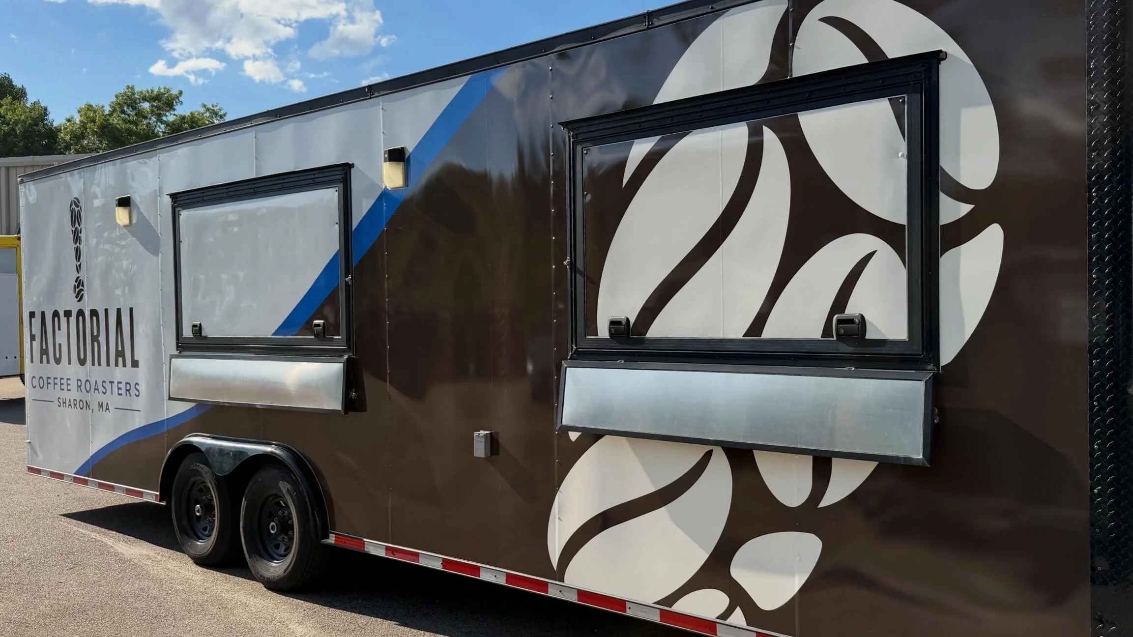 A coffee truck named 'Factoryal Coffee Roasters' parked outdoors on a sunny day, with coffee service windows and a decorative white and brown design on its exterior.