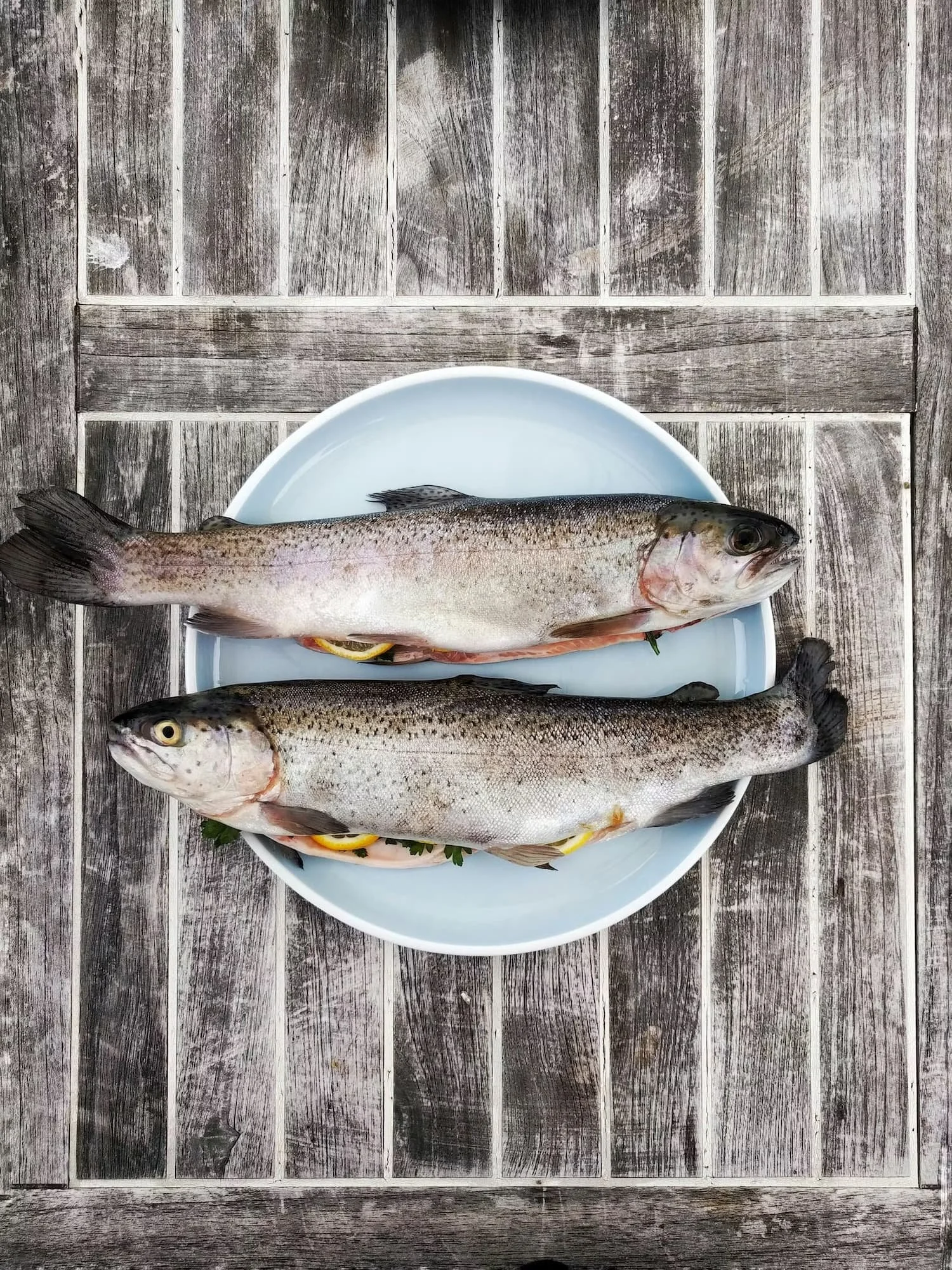 Two fish on a white plate placed on a wooden surface.