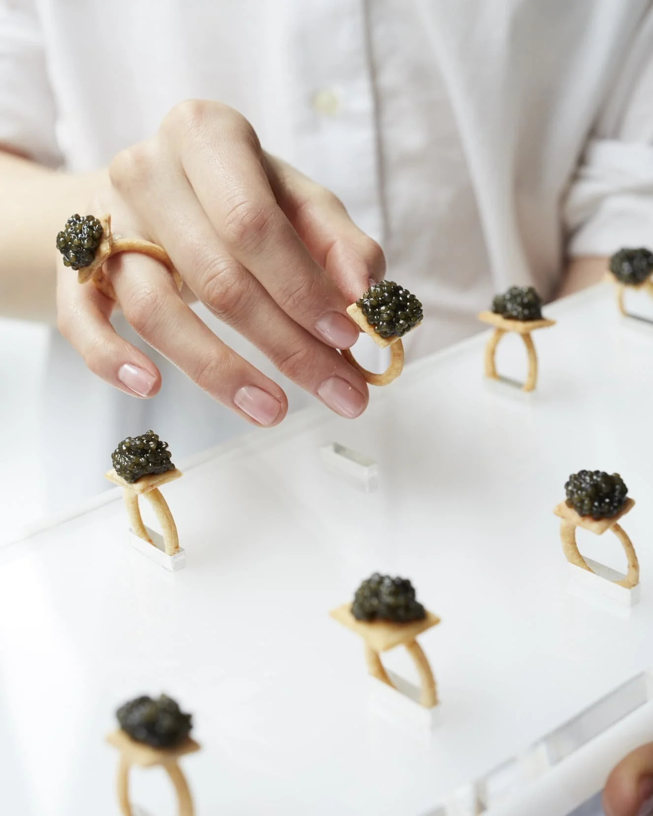 Person wearing edible rings with black caviar, holding a a tray of other similar edible rings with black caviar on a serving tray.