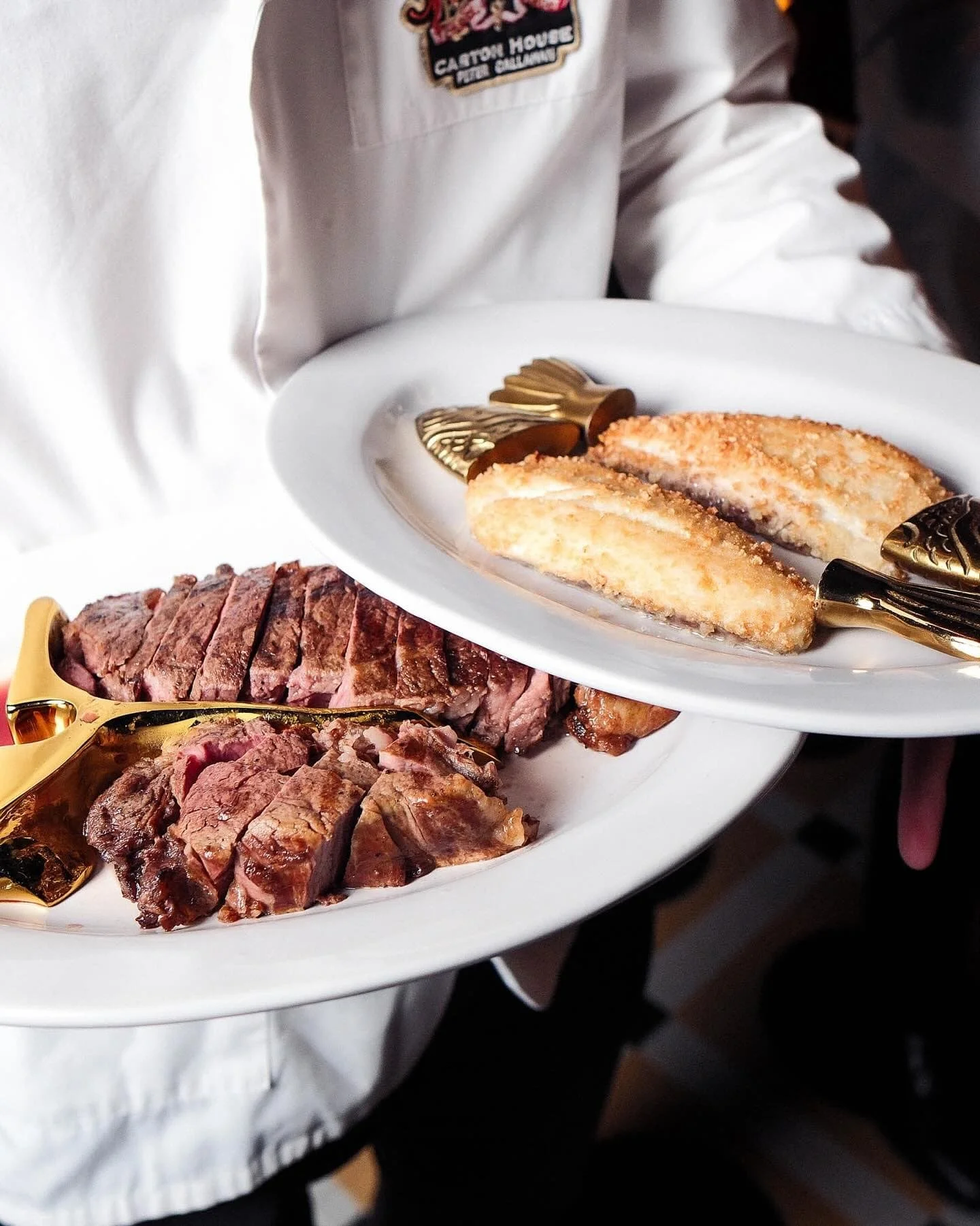 A white oval plate with sliced cooked steak and two breaded chicken cutlets, served with ornate gold-colored utensils. A server in a white shirt with a Carton House patch is holding the plate.