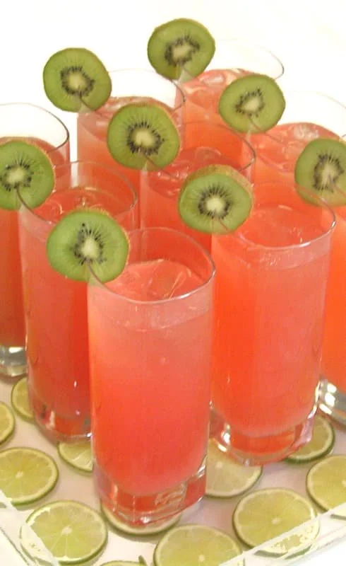 Tall glasses of watermelon margaritas garnished with a slice of kiwi on the rim, placed on a tray with lemon slices underneath.