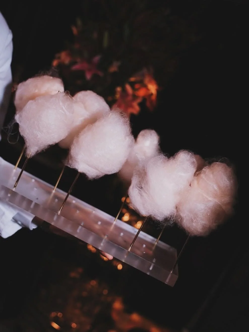 Pink cotton candy on sticks being held with a dark background and some pink flowers.