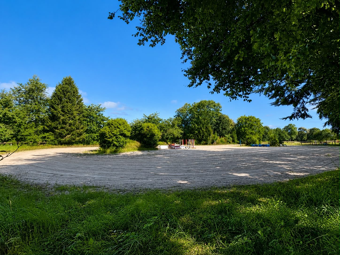 Un terrain de sport en plein air avec des arbres verts en arrière-plan, un ciel bleu clair et quelques structures de jeu ou équipements sportifs au centre.