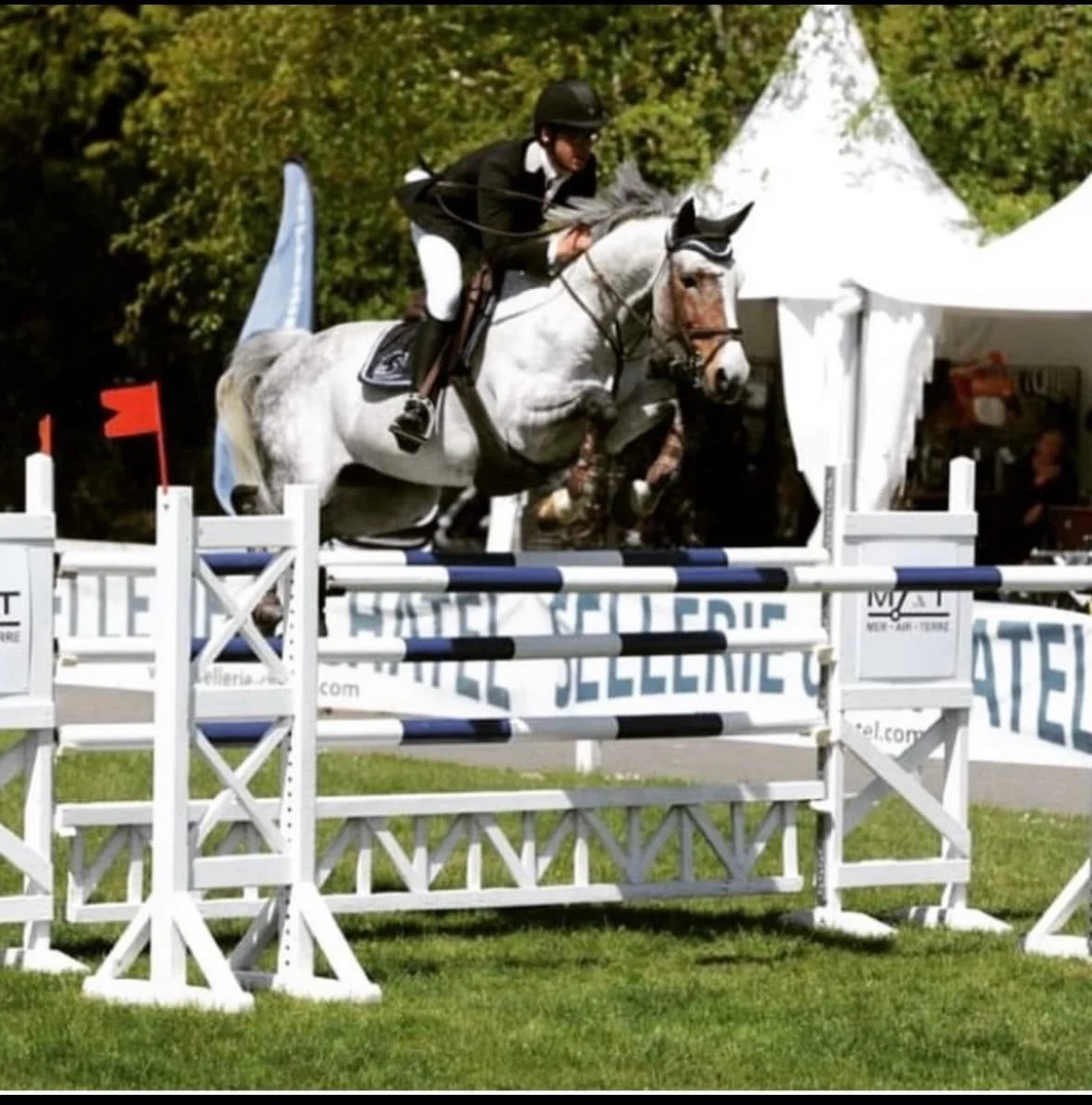 Un cavalier en tenue de compétition sautant une obstacle lors d'une épreuve d'équitation.