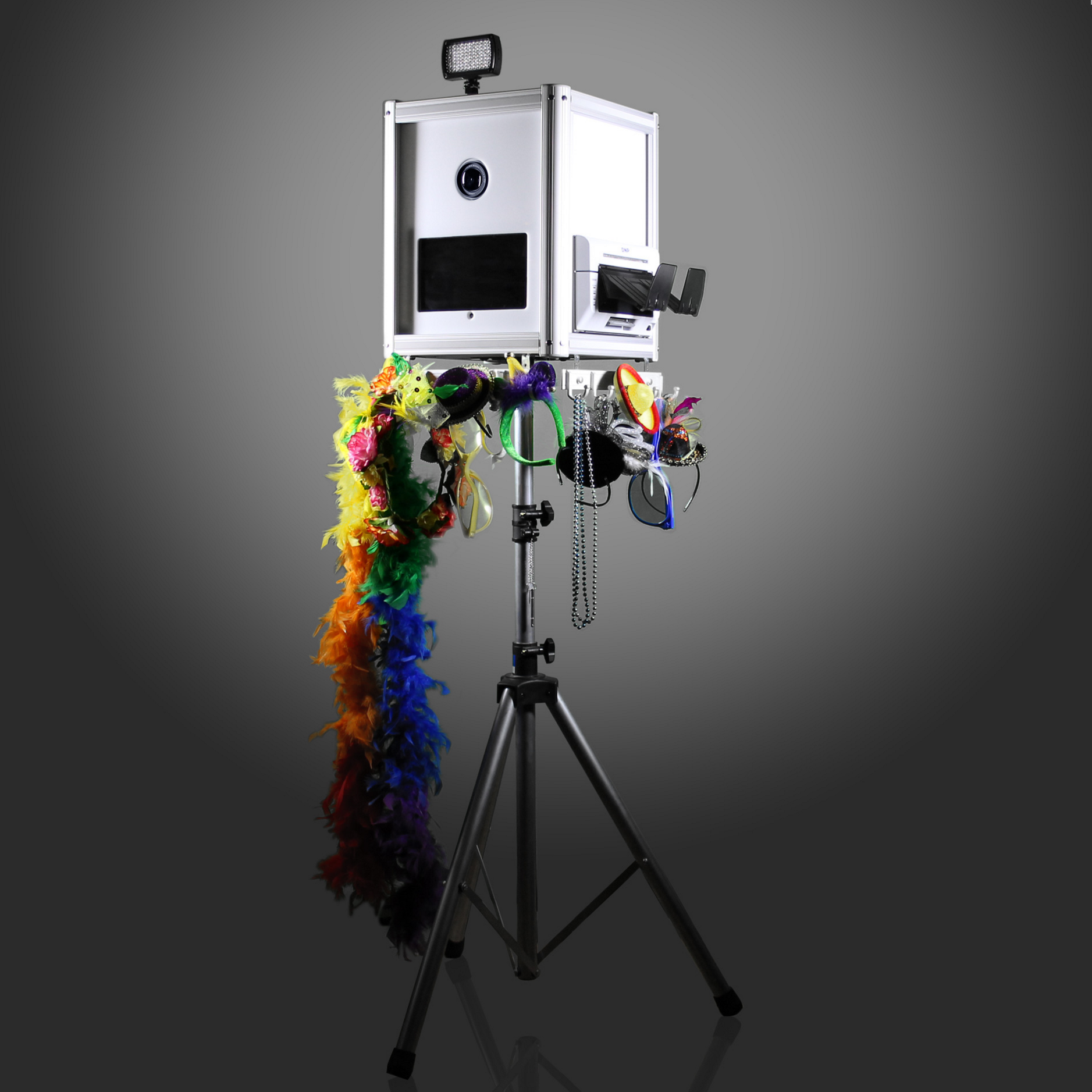 Photo of a photo booth with colorful feather boas, masks, and accessories hanging on a stand in front of a plain gray background.