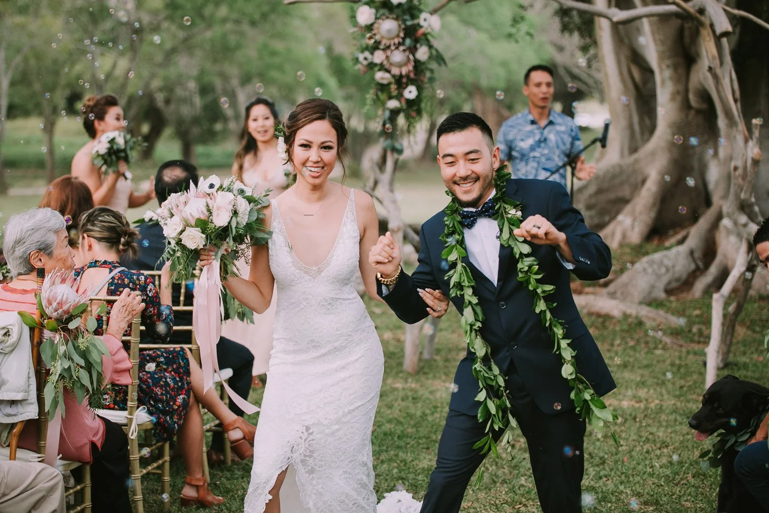 Bride and groom smiling and celebrating at their outdoor wedding reception, with guests seated and enjoying the event.