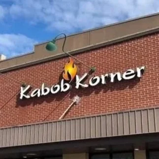Broken sign of a restaurant called Kabob Korner with a flaming grill image and a lamp hanging from the wall.