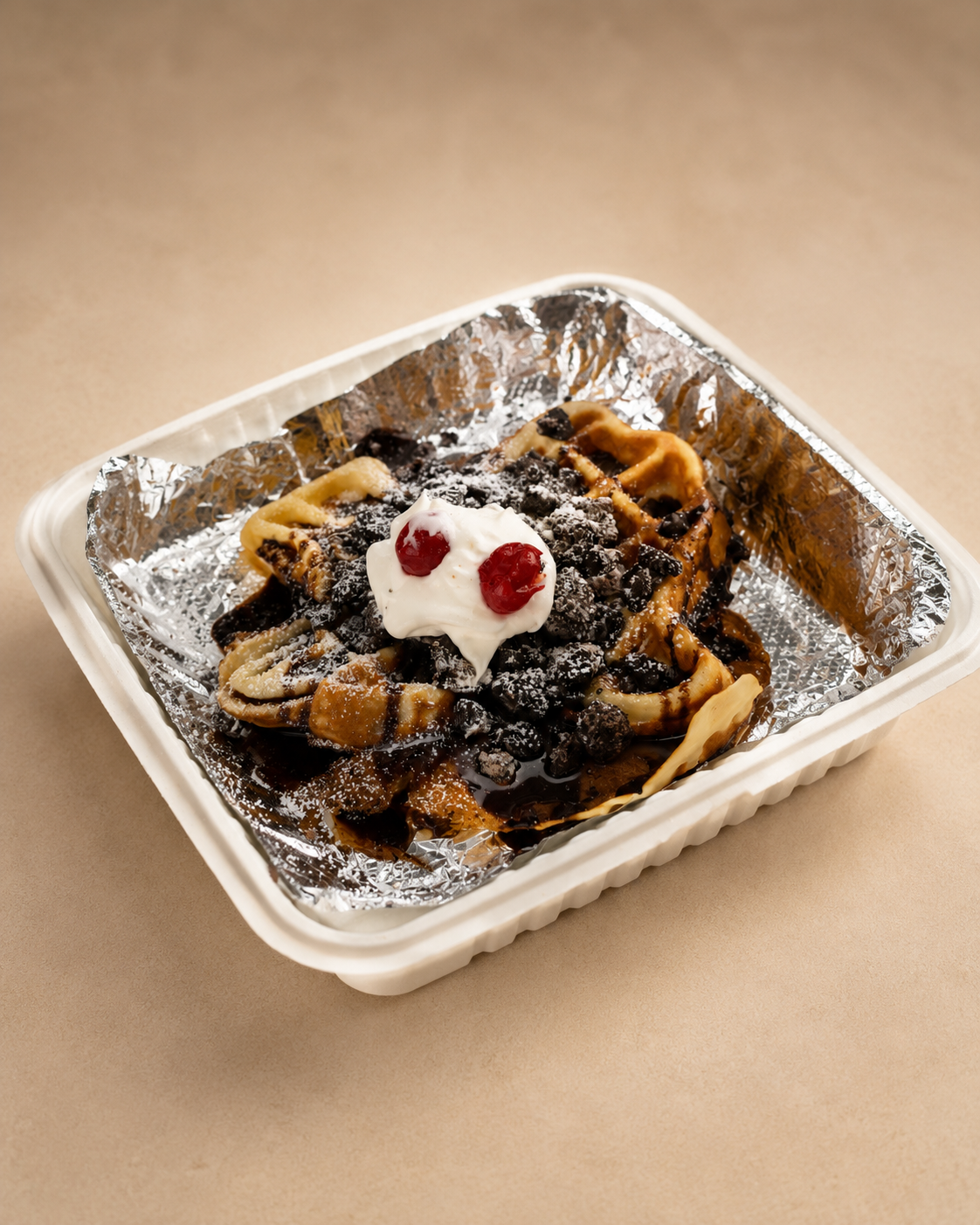 A serving of waffles topped with whipped cream, cherries, and chocolate syrup, served on a disposable tray lined with aluminum foil.