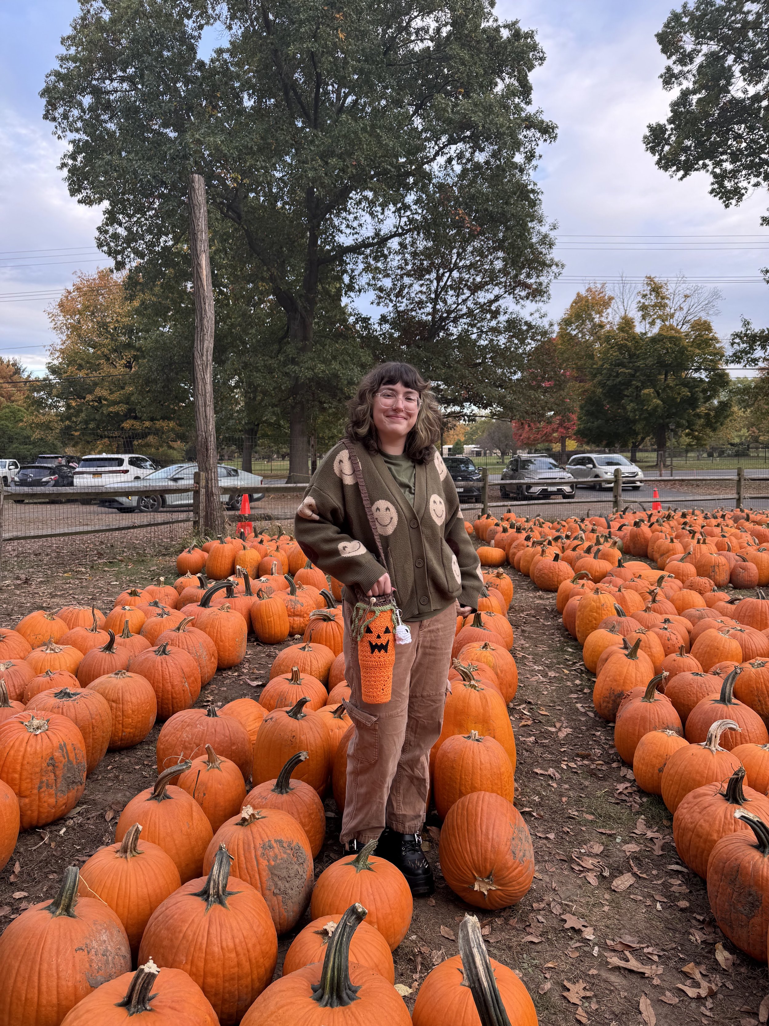 Me standing in a pumpkin patch, with a handmade jack-o-lantern crochet bag.