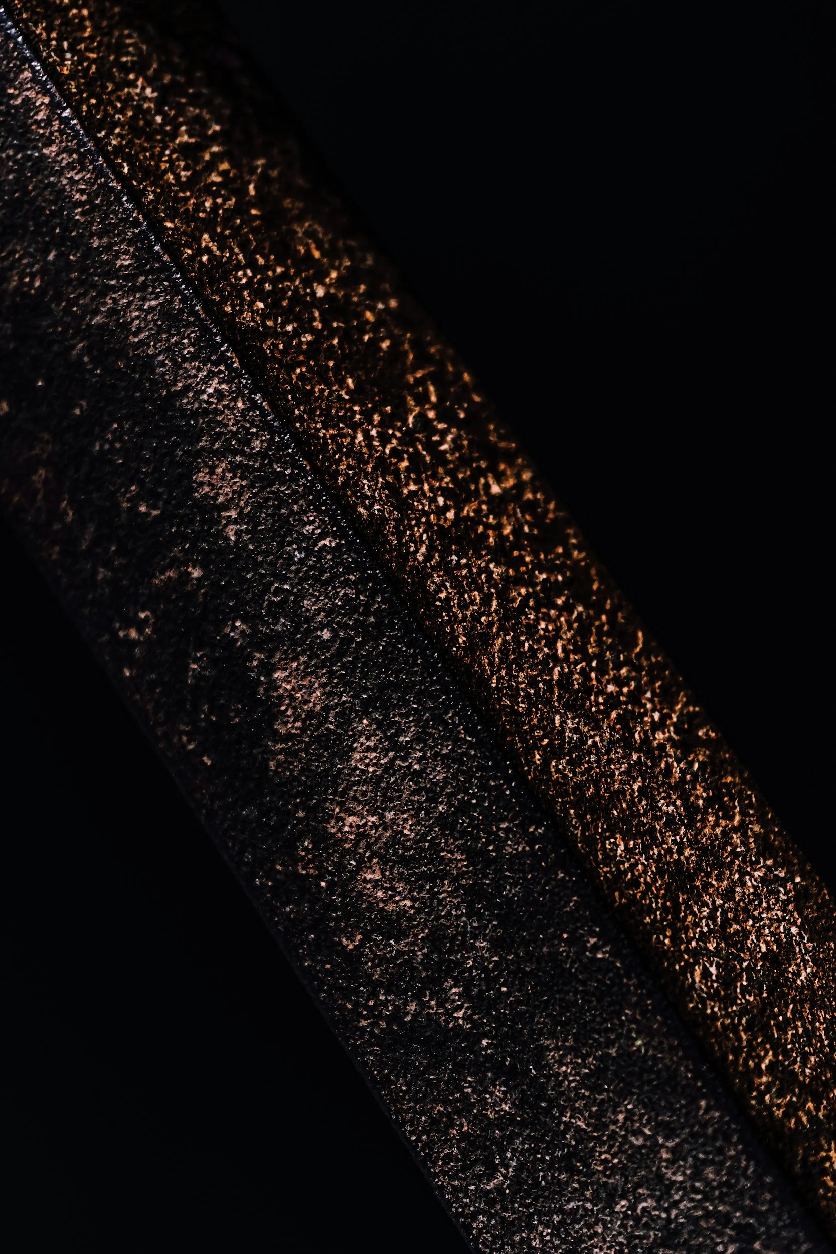 Close-up of a textured, dark surface with a diagonal strip of warm, glittering particles or light reflections.