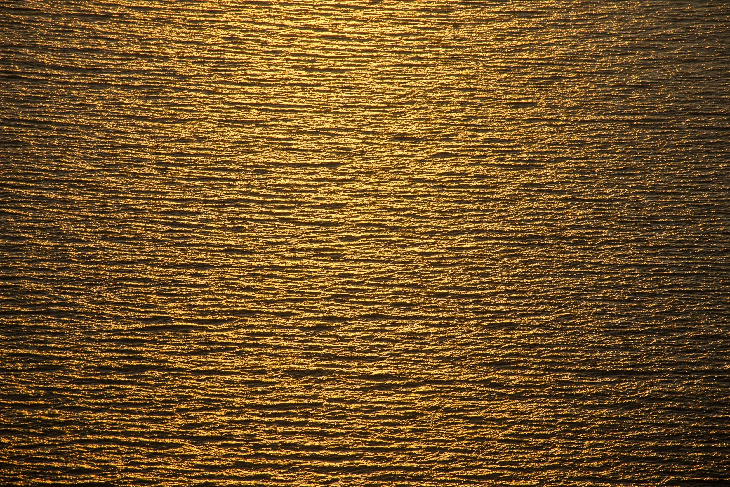 Golden sunset reflecting on the surface of a body of water with ripples.
