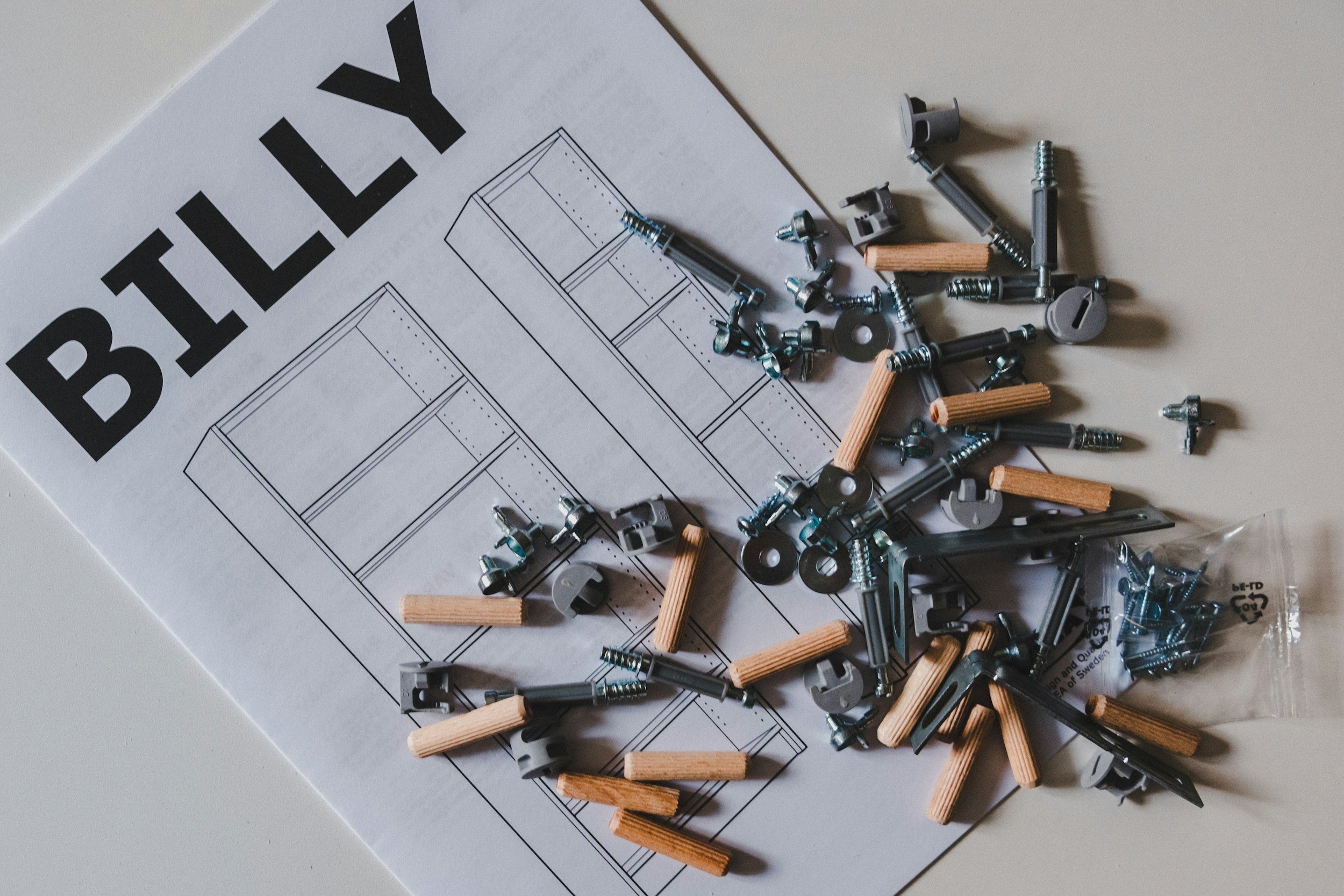 A partially assembled piece of furniture with screws, wooden dowels, and various hardware parts scattered on top of an instruction sheet labeled 'BLY'.