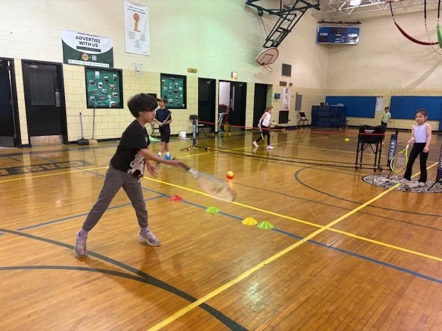 Children playing badminton and other sports in a school gymnasium.