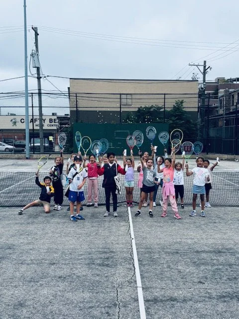 Children and adults holding tennis rackets on a tennis court