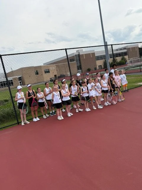 Group of young girls in tennis uniforms holding tennis rackets on a tennis court