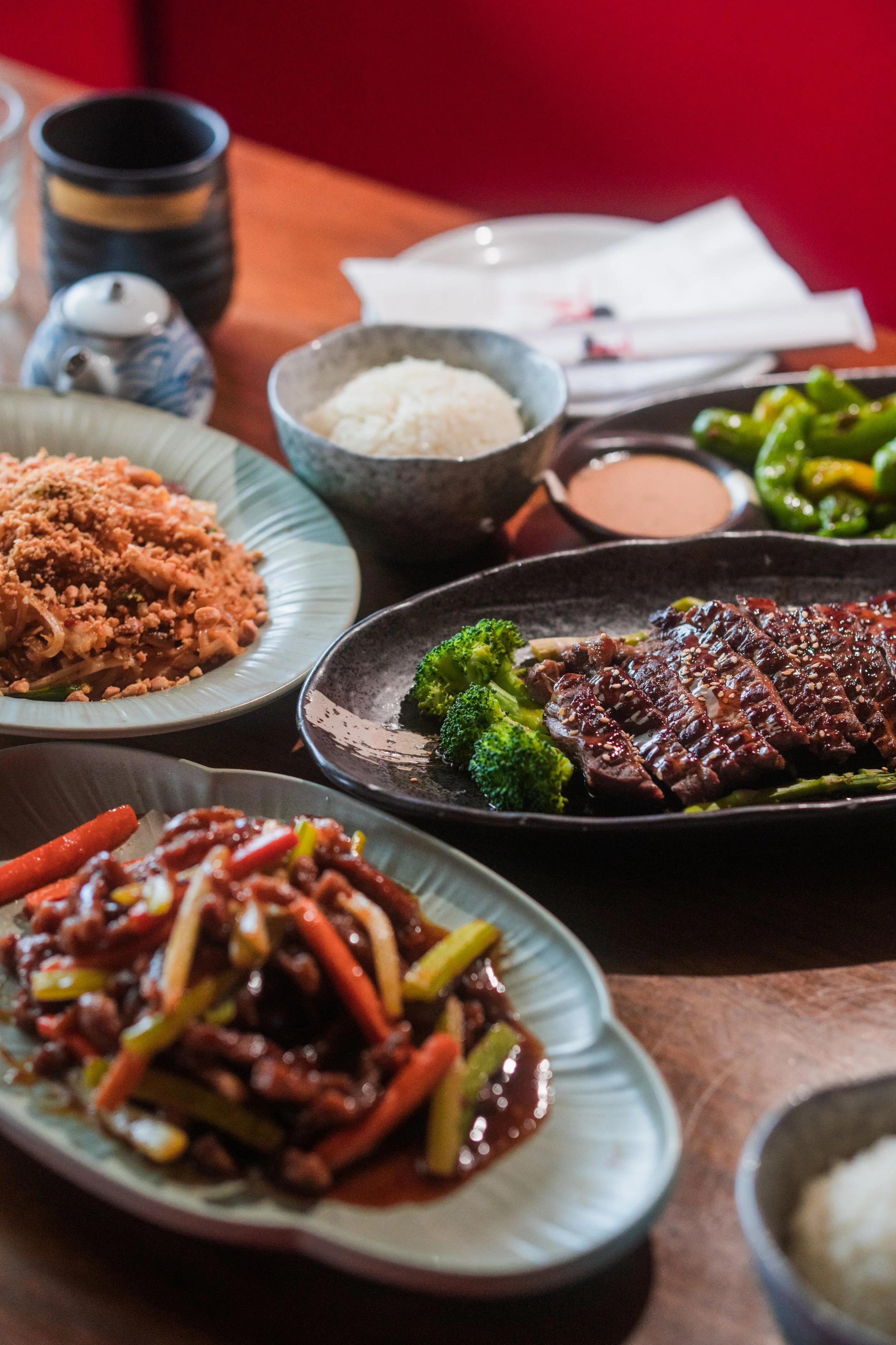 Assorted Asian dishes on a table, including a plate of stir-fried beef with broccoli, a bowl of rice, and a plate of sautéed vegetables with sauce.