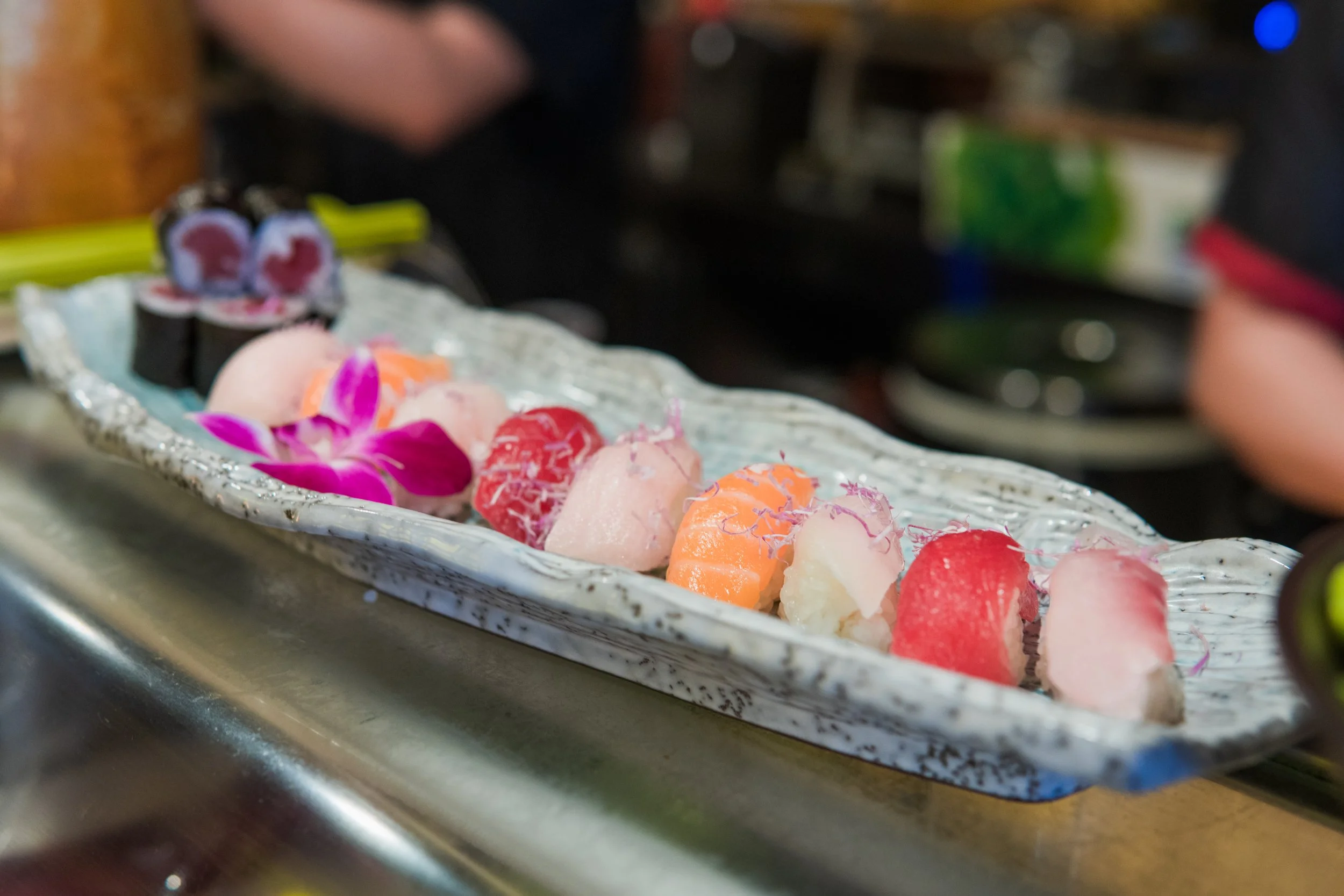 A silver platter with pink, orange, and red ice cream scoops garnished with a pink orchid flower, set on a kitchen countertop.