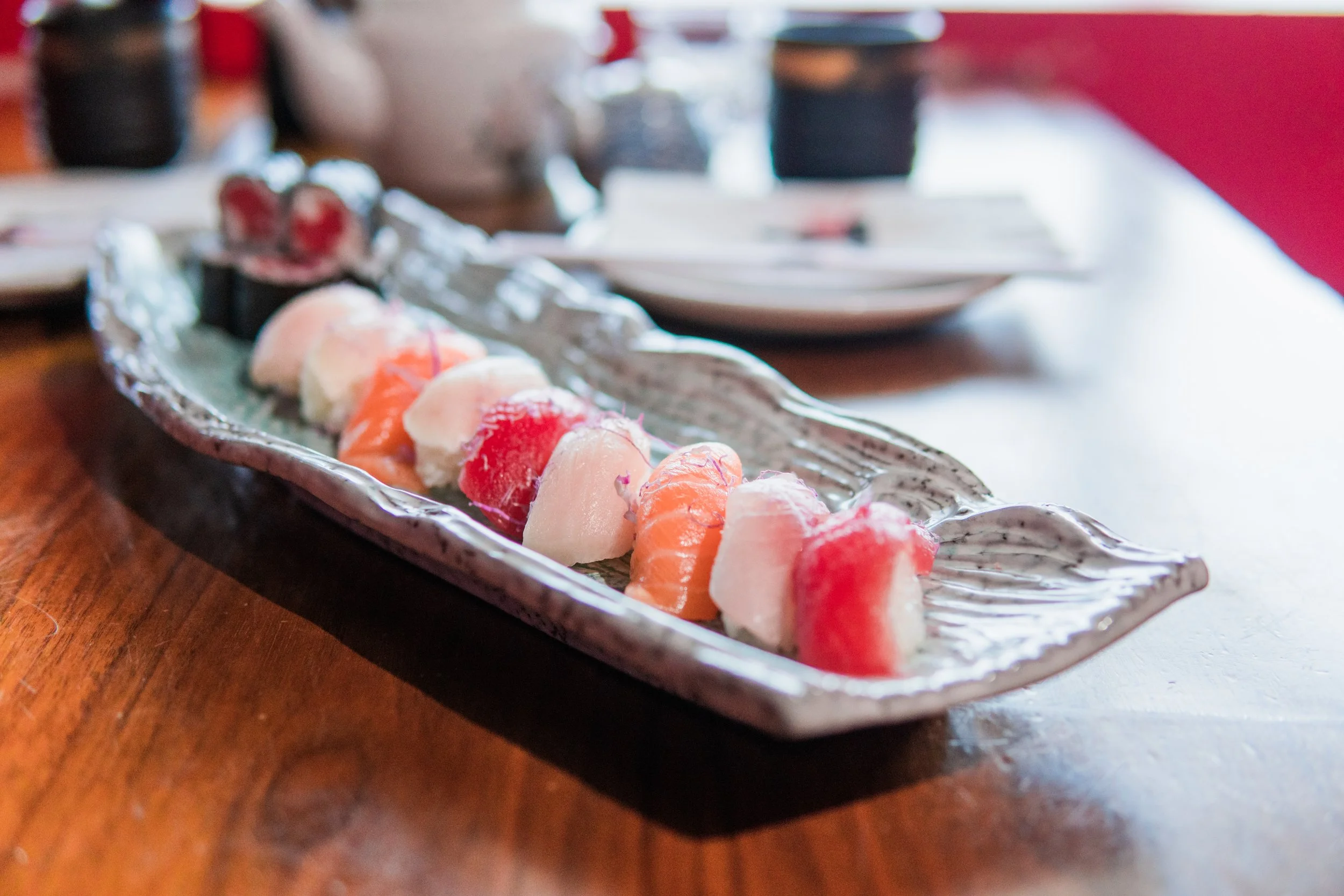 A silver serving tray with assorted sliced sashimi fish, placed on a wooden table.