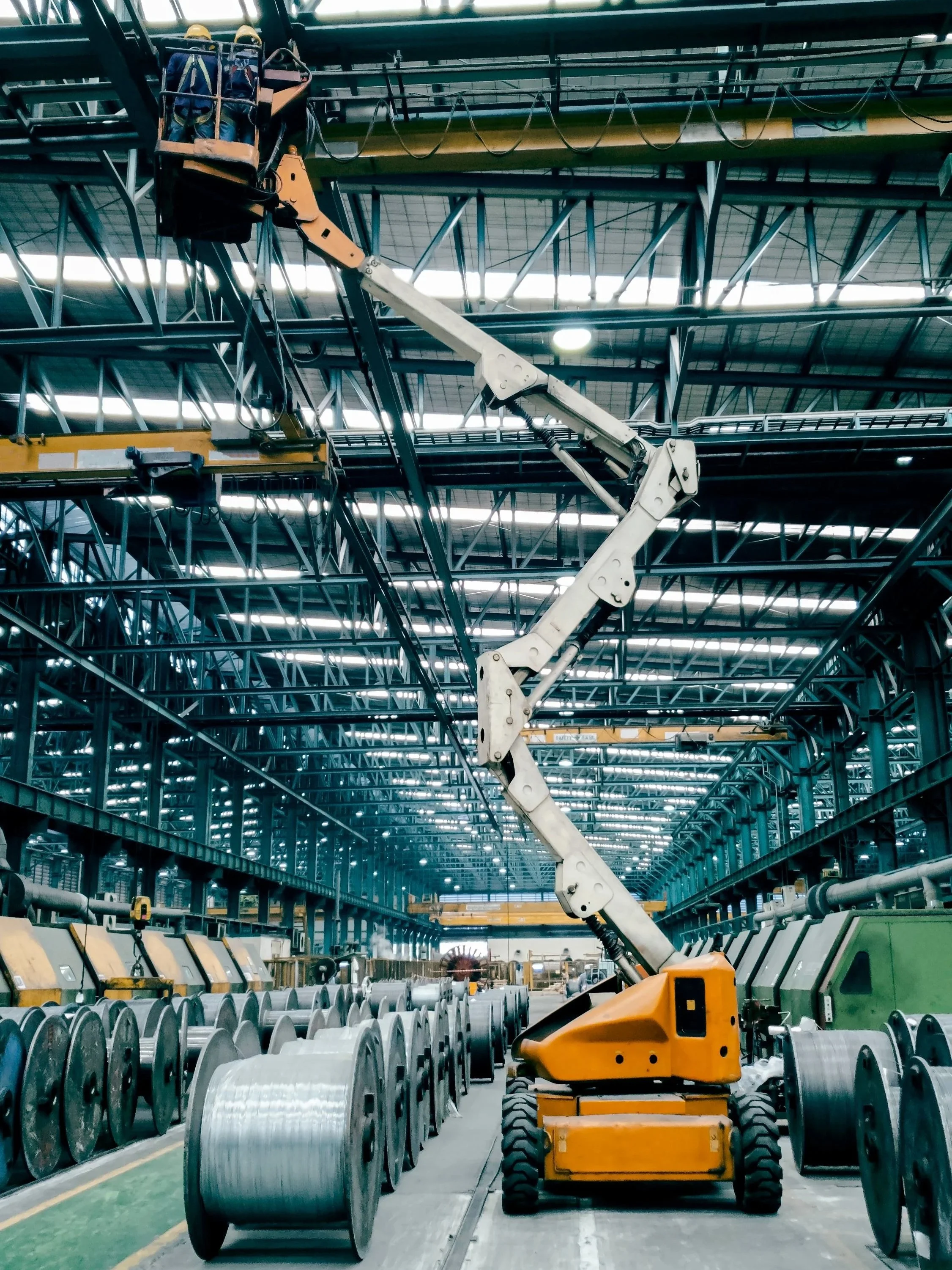Overhead crane maintenance being performed by technician on lift.