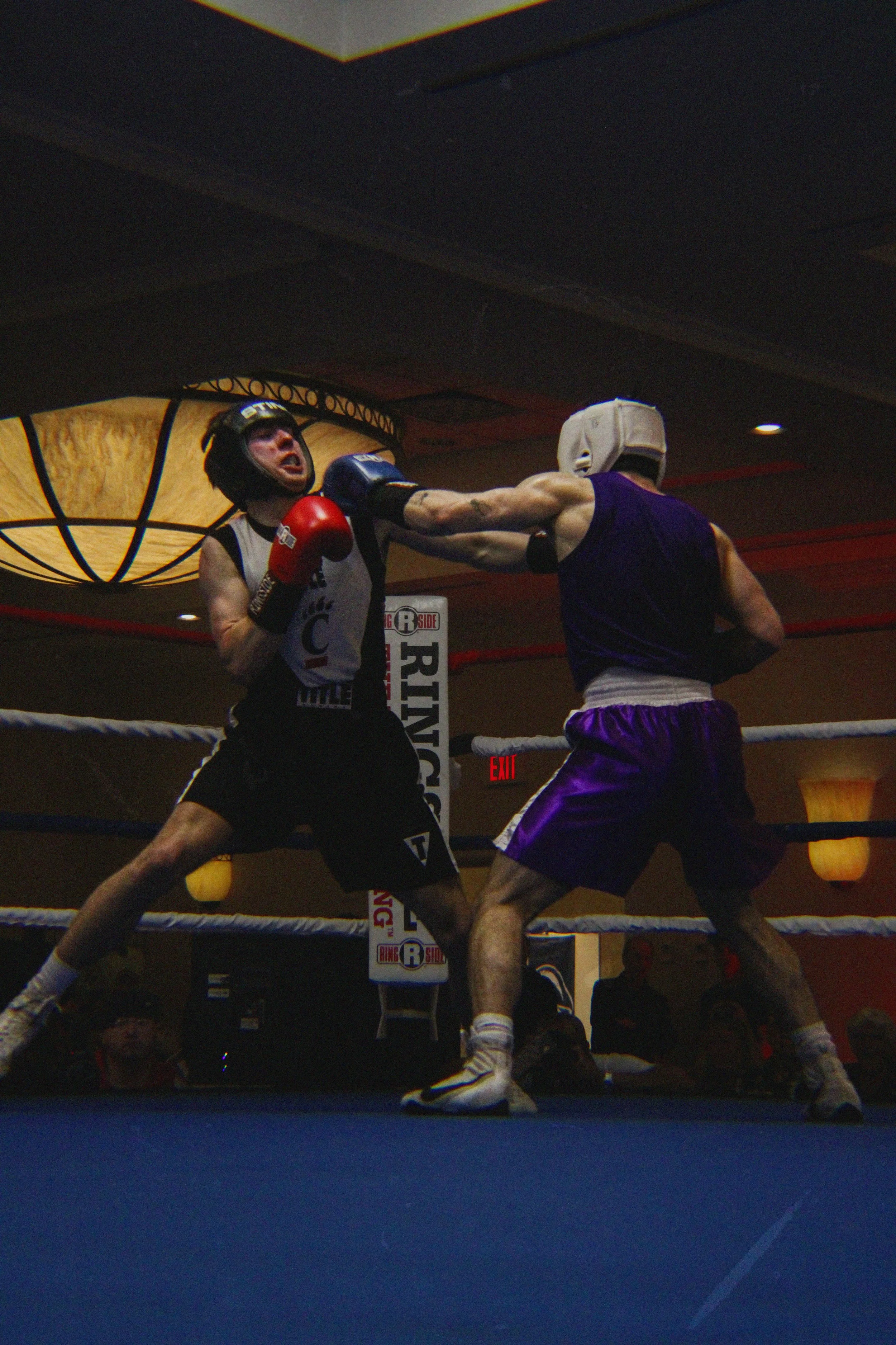 Two male boxers wearing protective headgear and gloves sparring in a boxing ring, with one delivering a punch to the other's face.