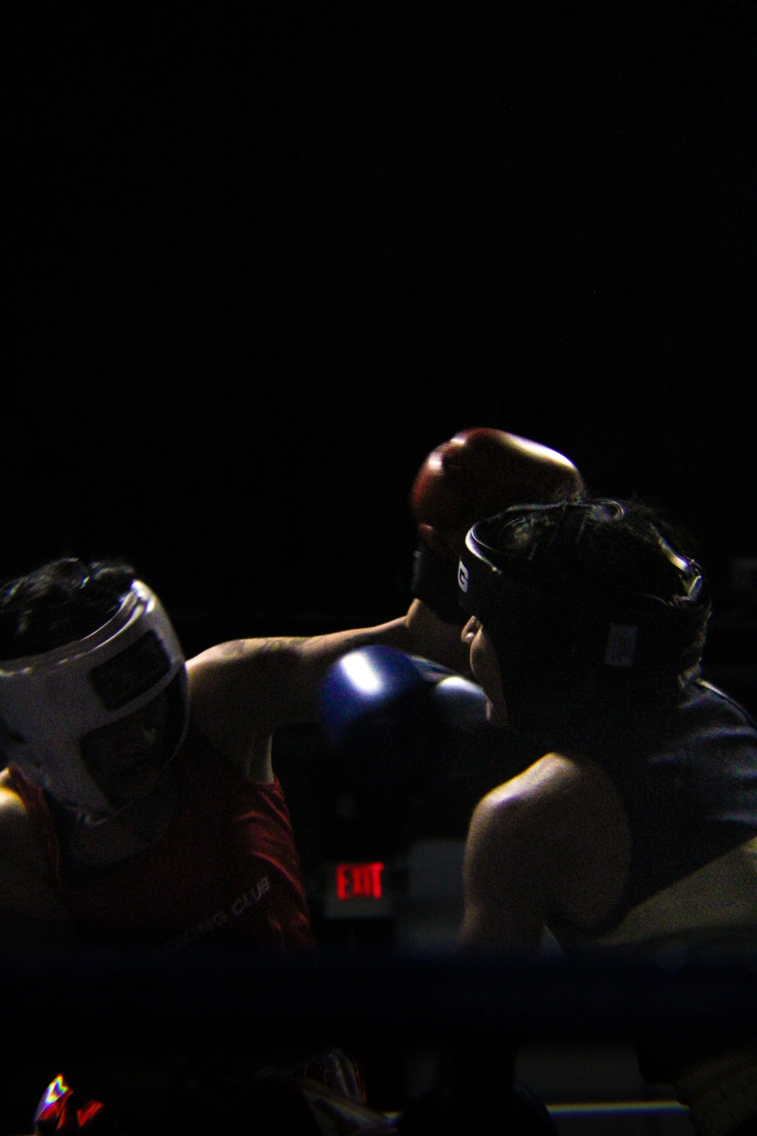 Several skateboards and skateboarders in the dark, with a dimly lit background and an exit sign visible.