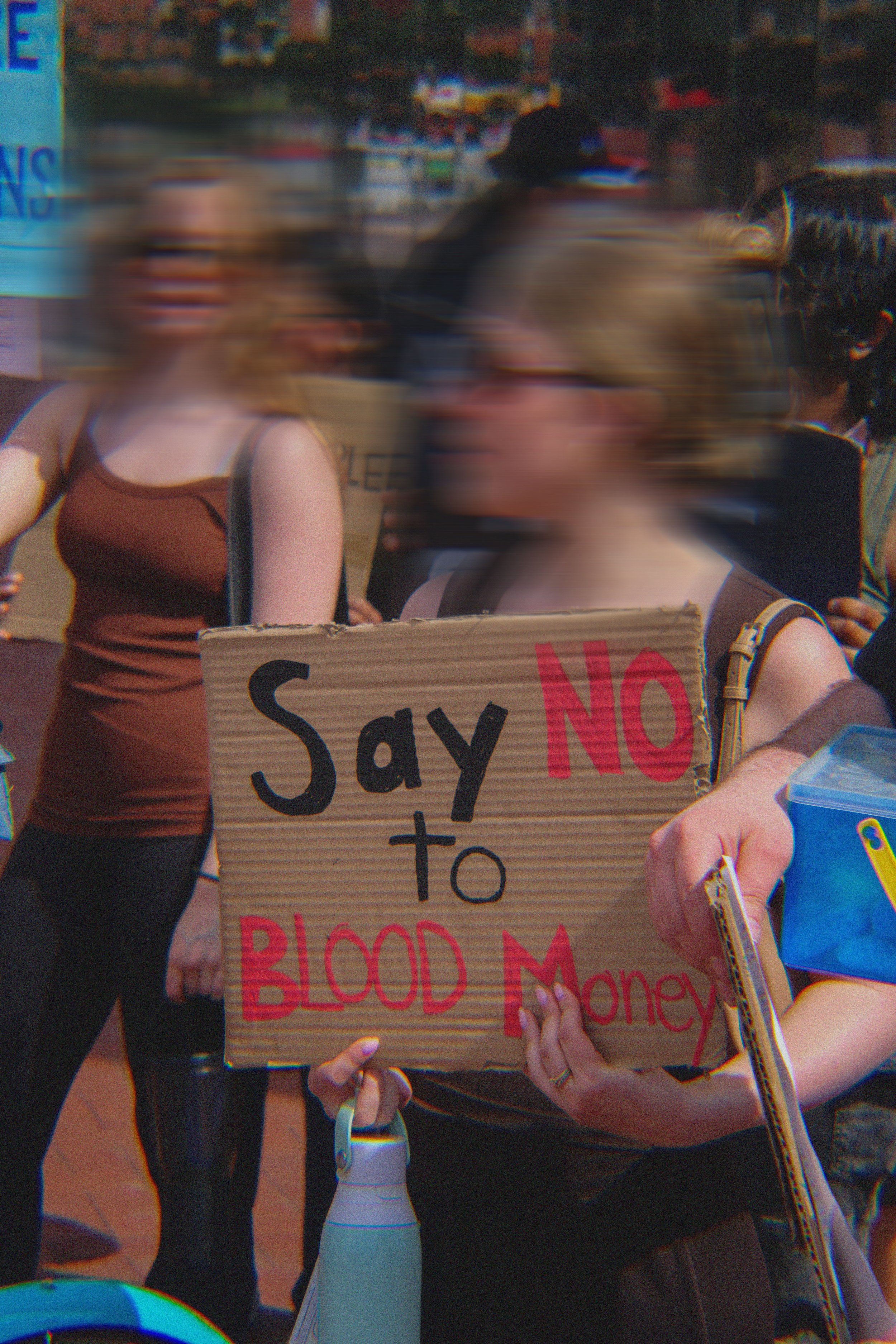 People participating in a protest holding signs and banners, with one sign reading 'Say NO to BLOOD Money'.