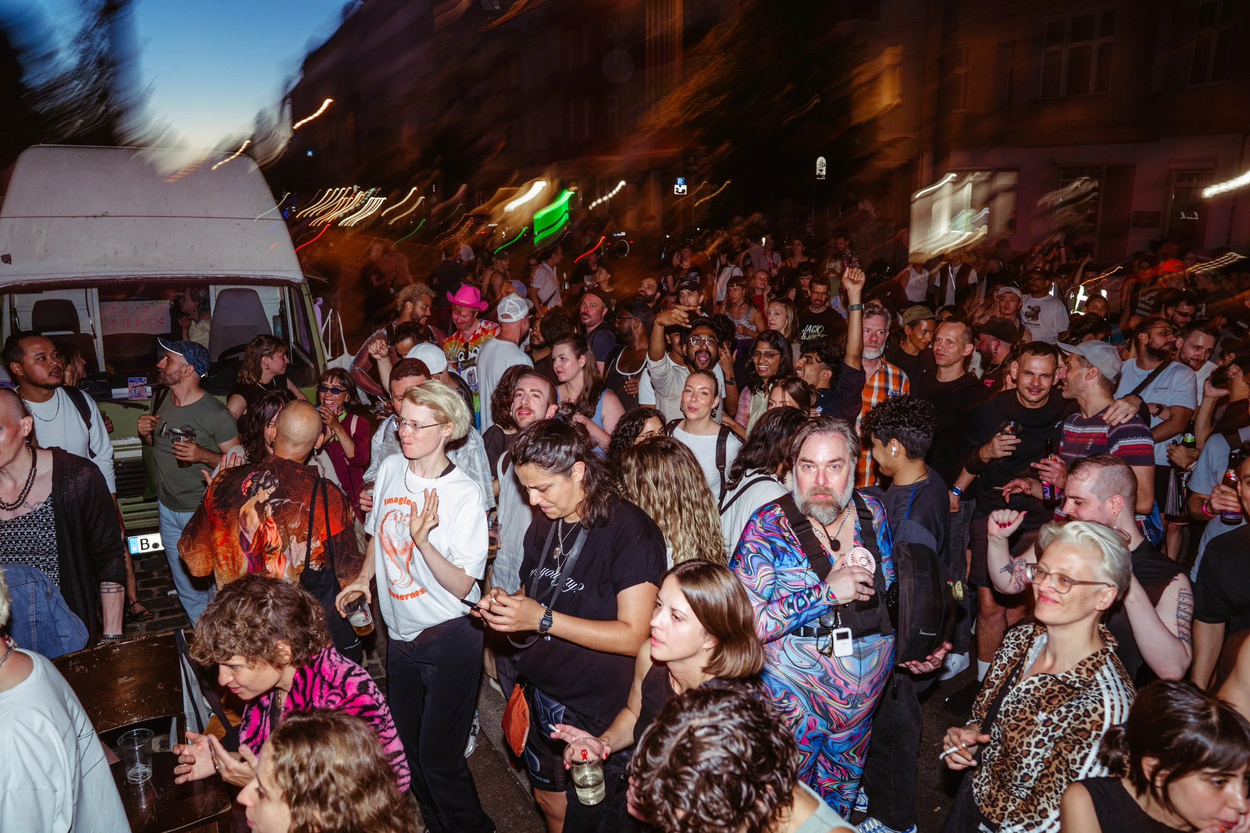 A large crowd of people gathered outdoors at night, enjoying a festive event with some dancing and socializing.