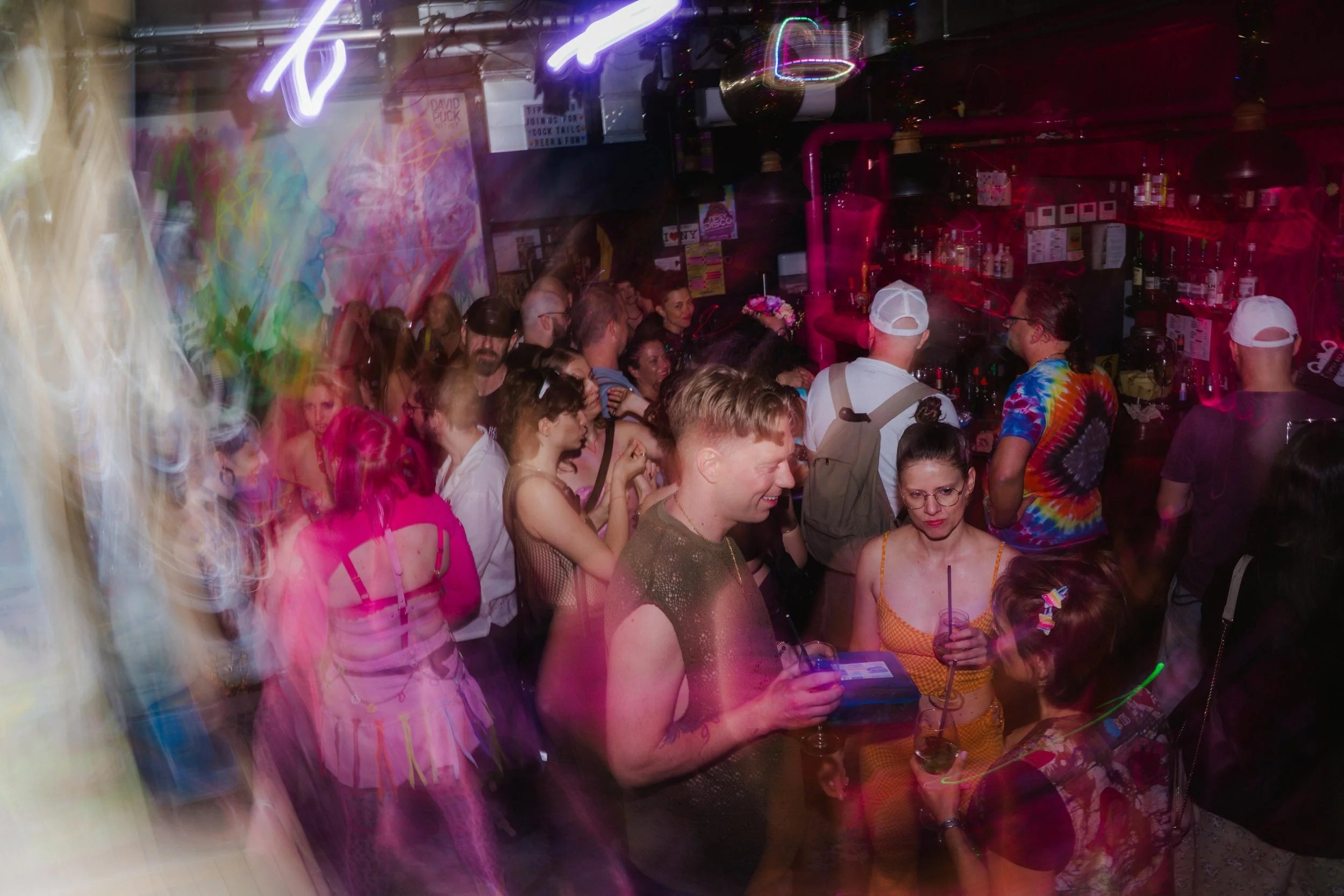 A crowded nightclub with people dancing and socializing under colorful neon and LED lighting.