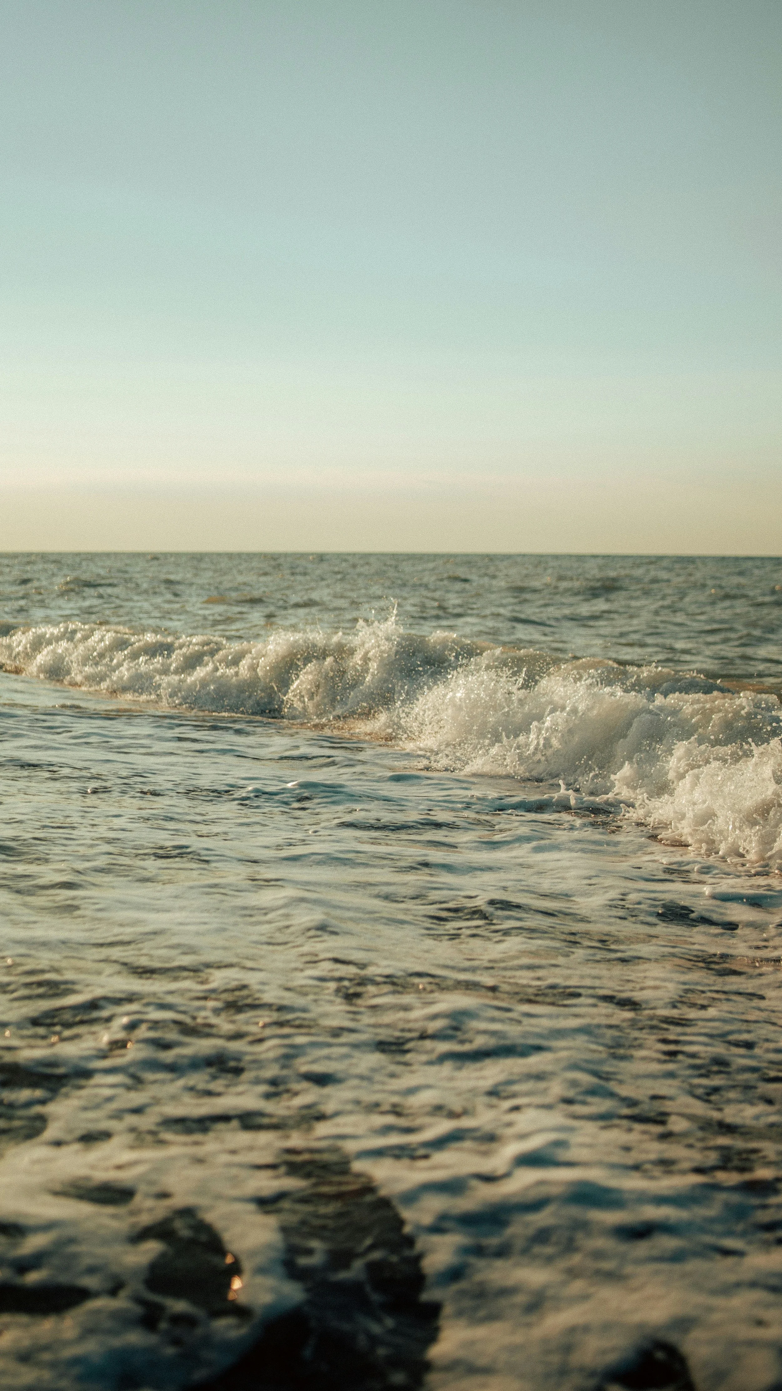 The image shows a calm ocean with gentle waves, under a clear sky with a faint gradient from light to darker blue, suggesting early morning or late afternoon.