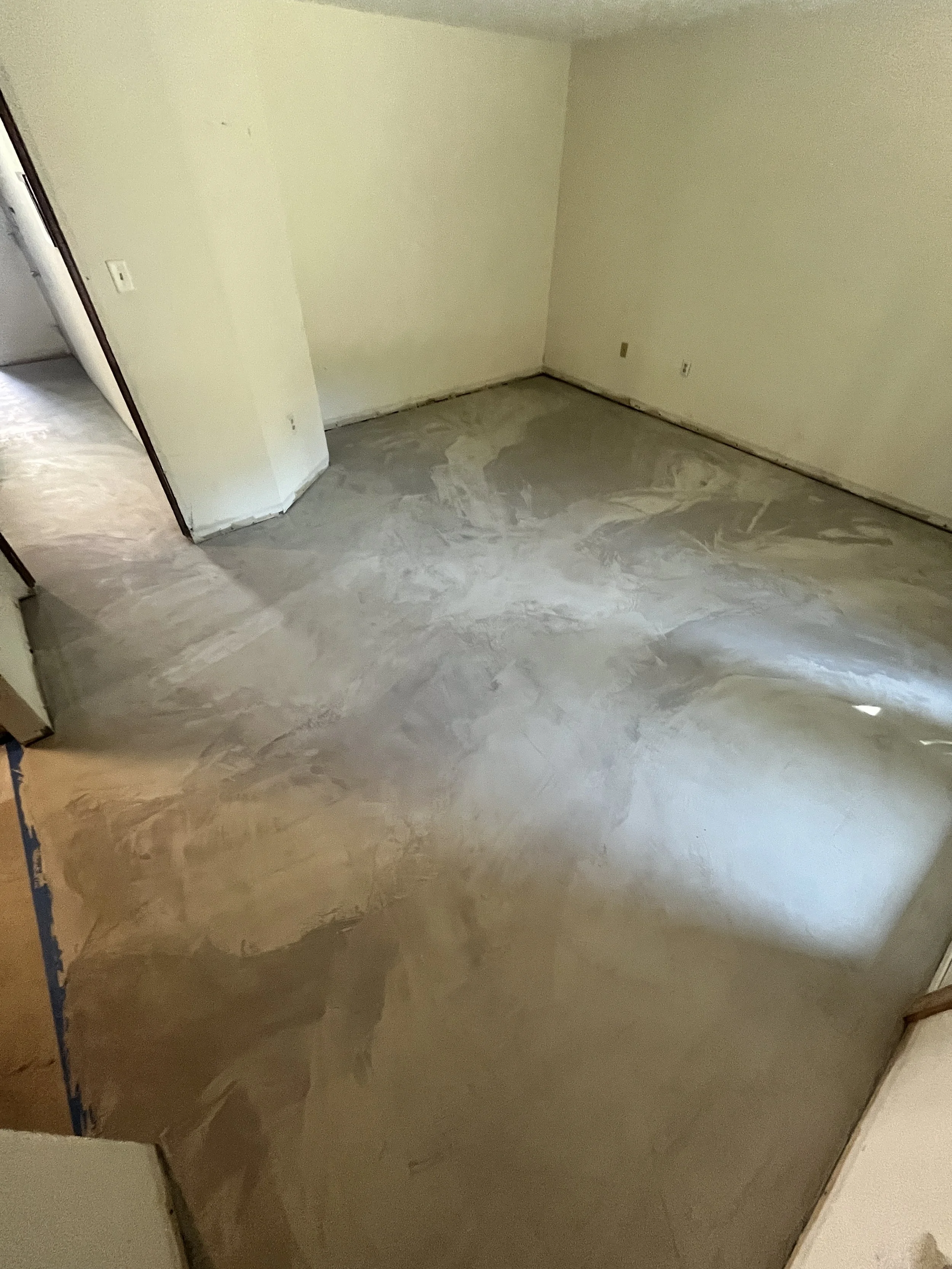 Empty room with a concrete floor, beige walls, and visible electrical outlets, with an open doorway leading to another space.
